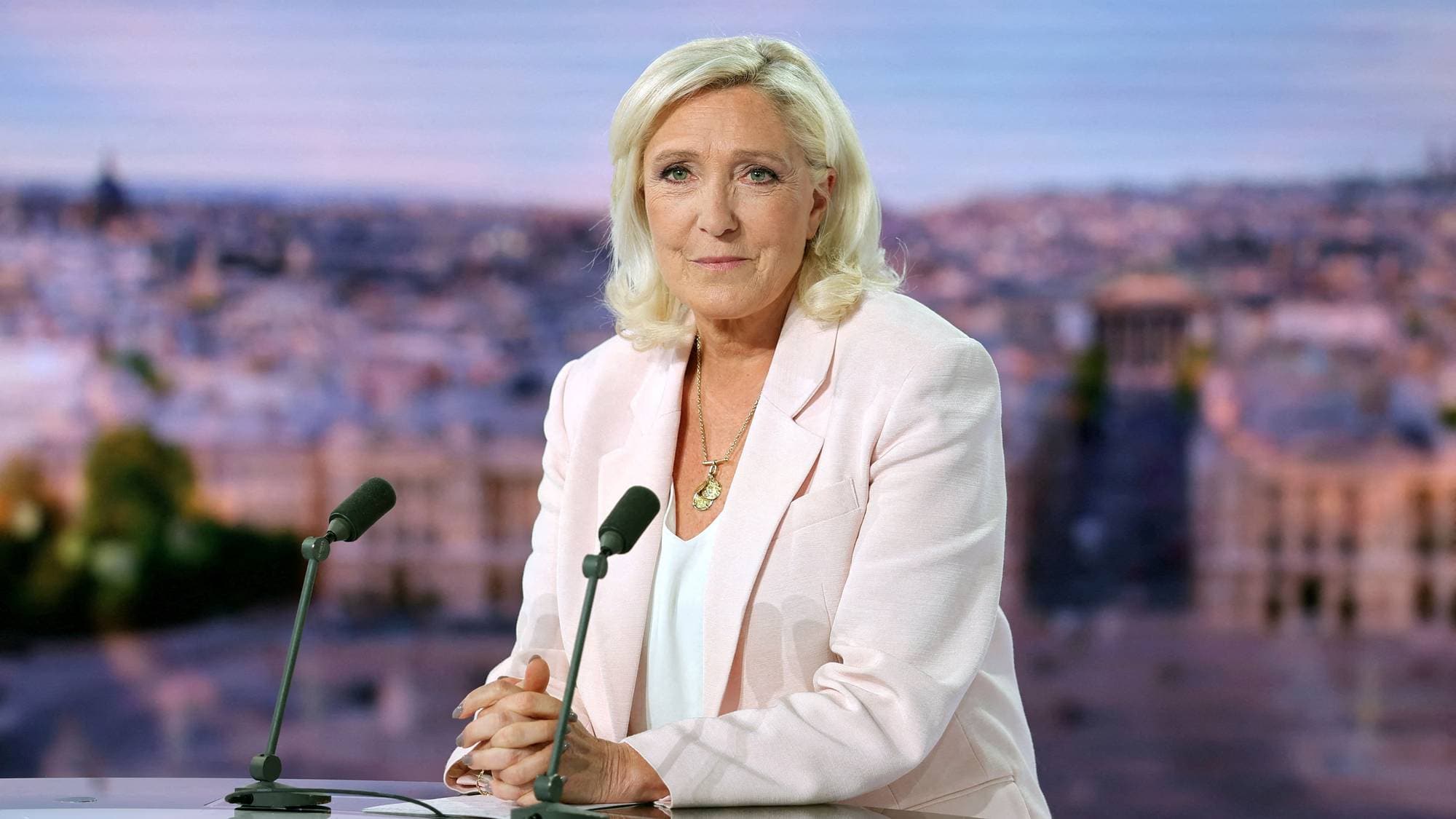 Marine Le Pen sitter ved et bord med mikrofoner foran en bakgrunn av Paris. 