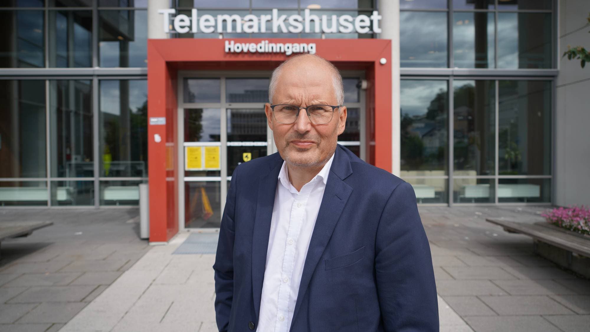 Mann ser rett i kamera i dressjakke. Han står utenfor Telemarkshuset.