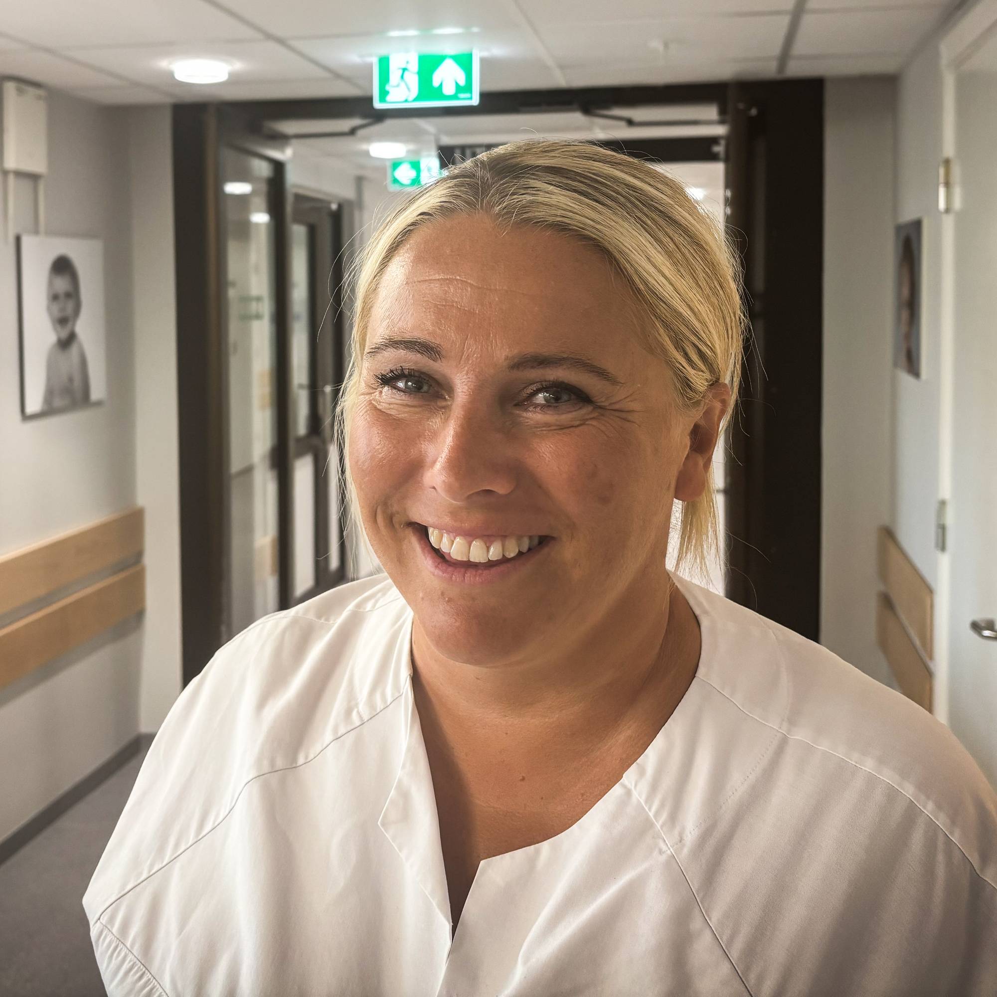 En person med hvite klær som smiler i en gang på sykehuset.