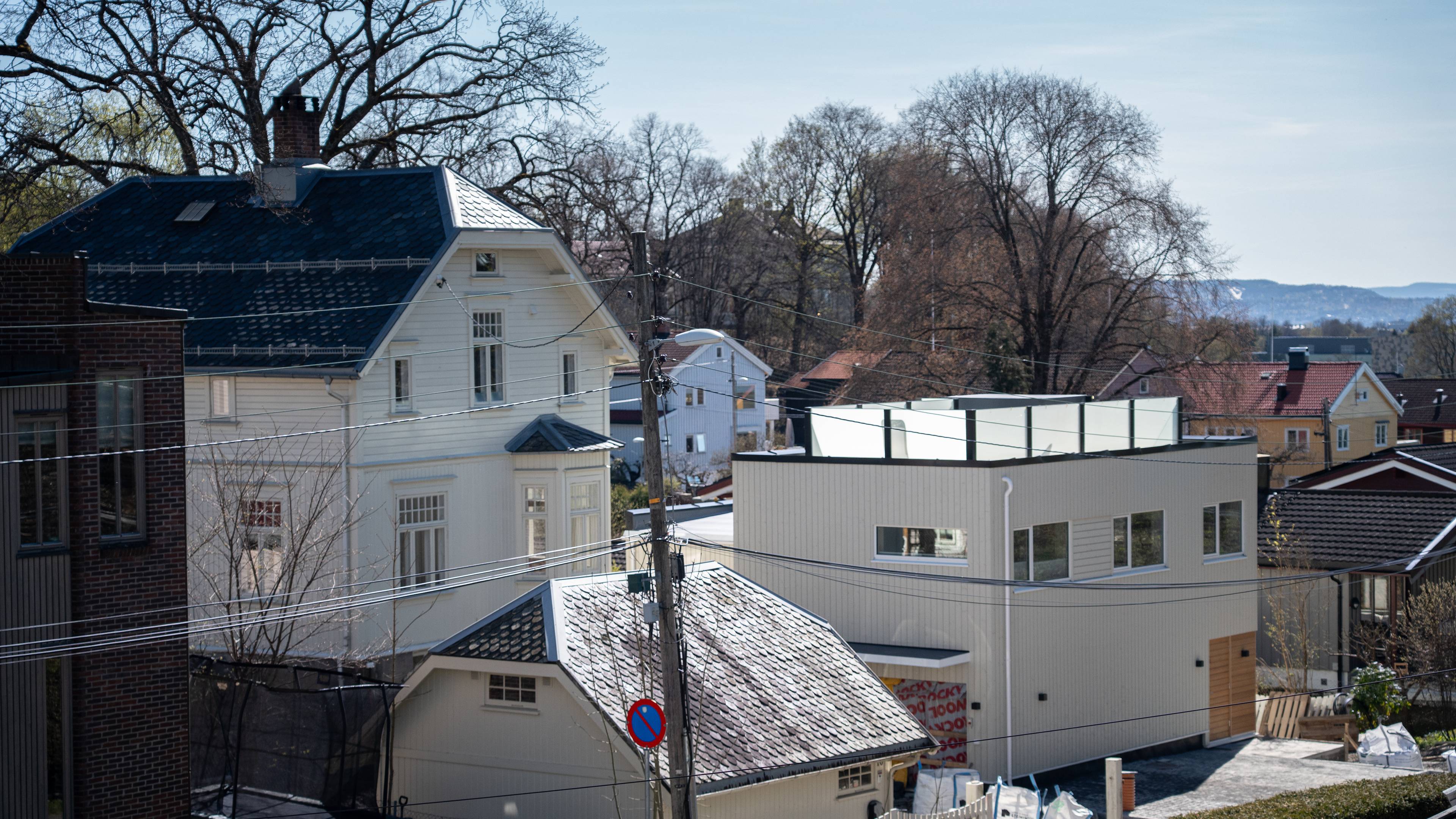 En rekke hus er synlige på en solrik dag. I forgrunnen ses en moderne bygning med vinduer og et flatt tak med glassrekkverk. Ved siden av står et eldre hvitt hus med saltak og pipe.