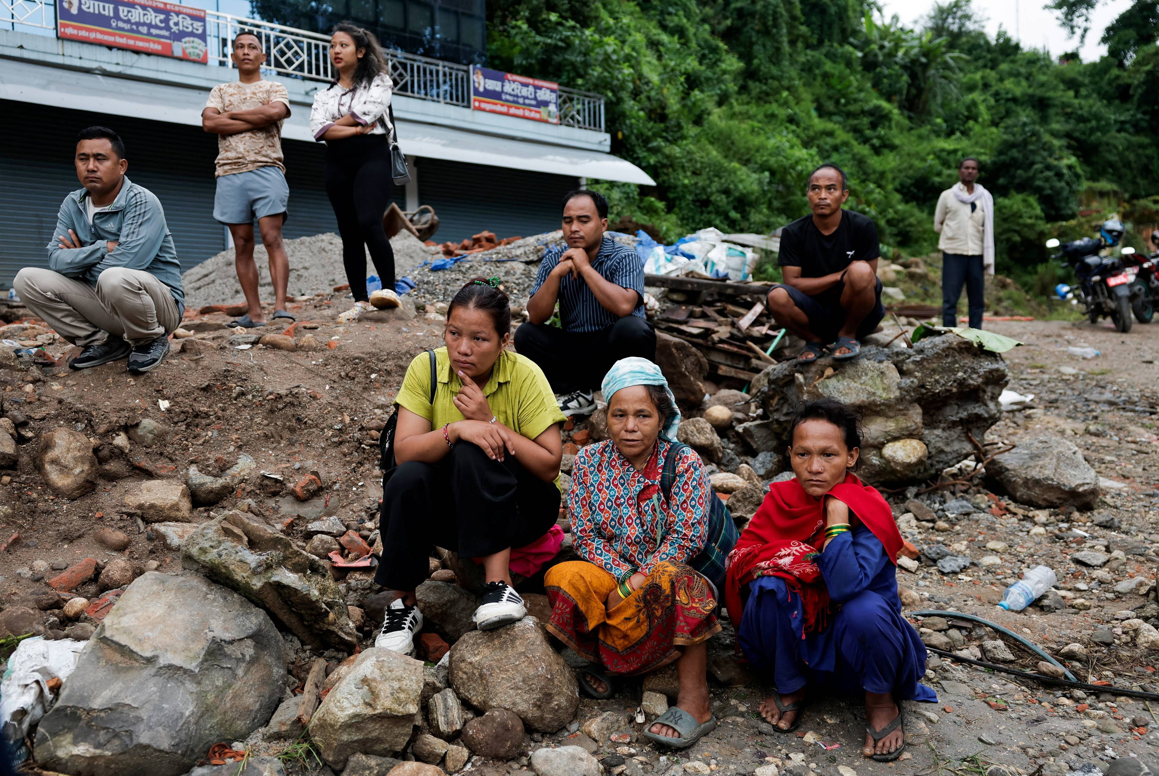 En gruppe mennesker sitter og står i et rasområde med stein og grus etter en flom i Nepal. (Bildebeskrivelsen er laget av en KI-tjeneste)