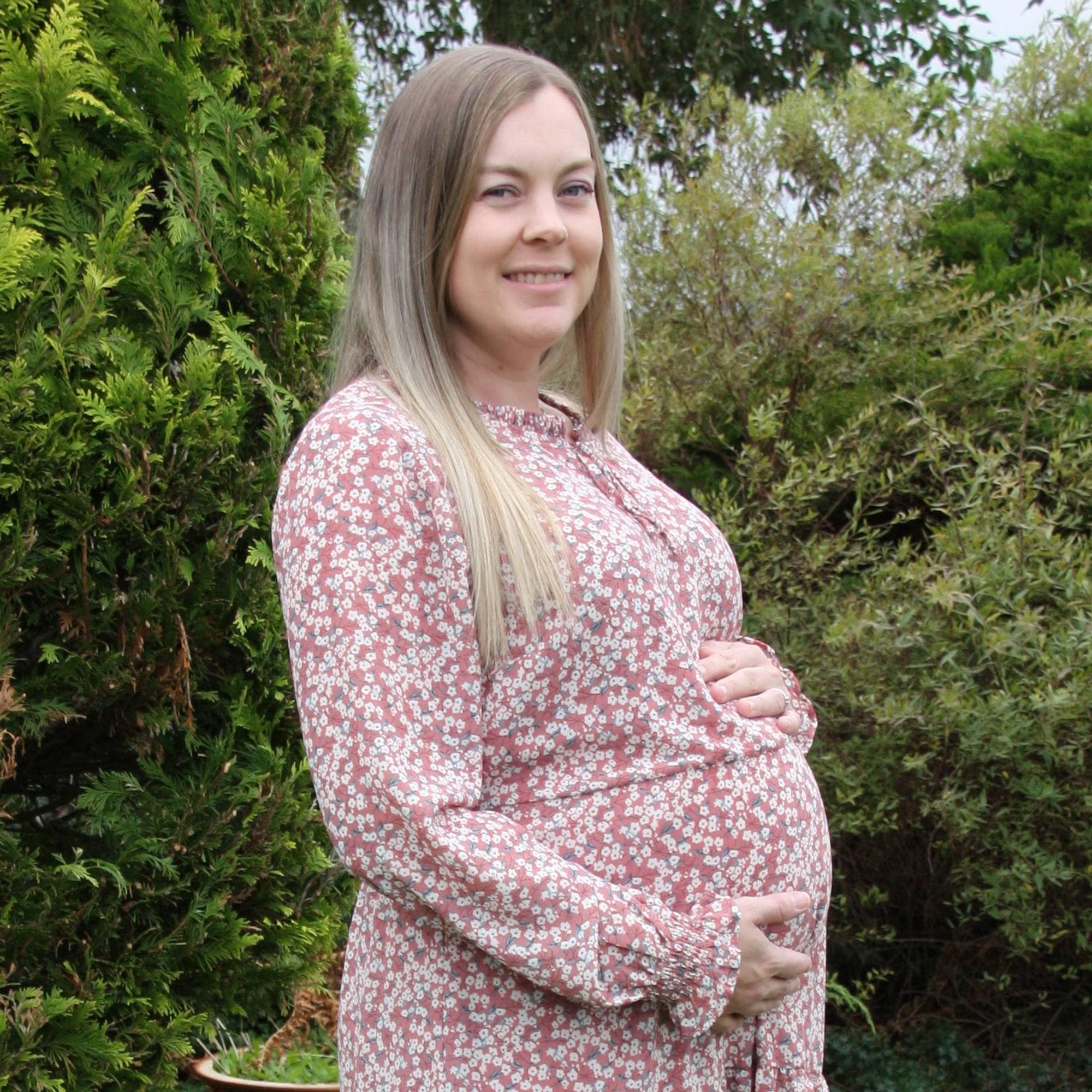 Gravid kvinne i en hage iført sommerkjole