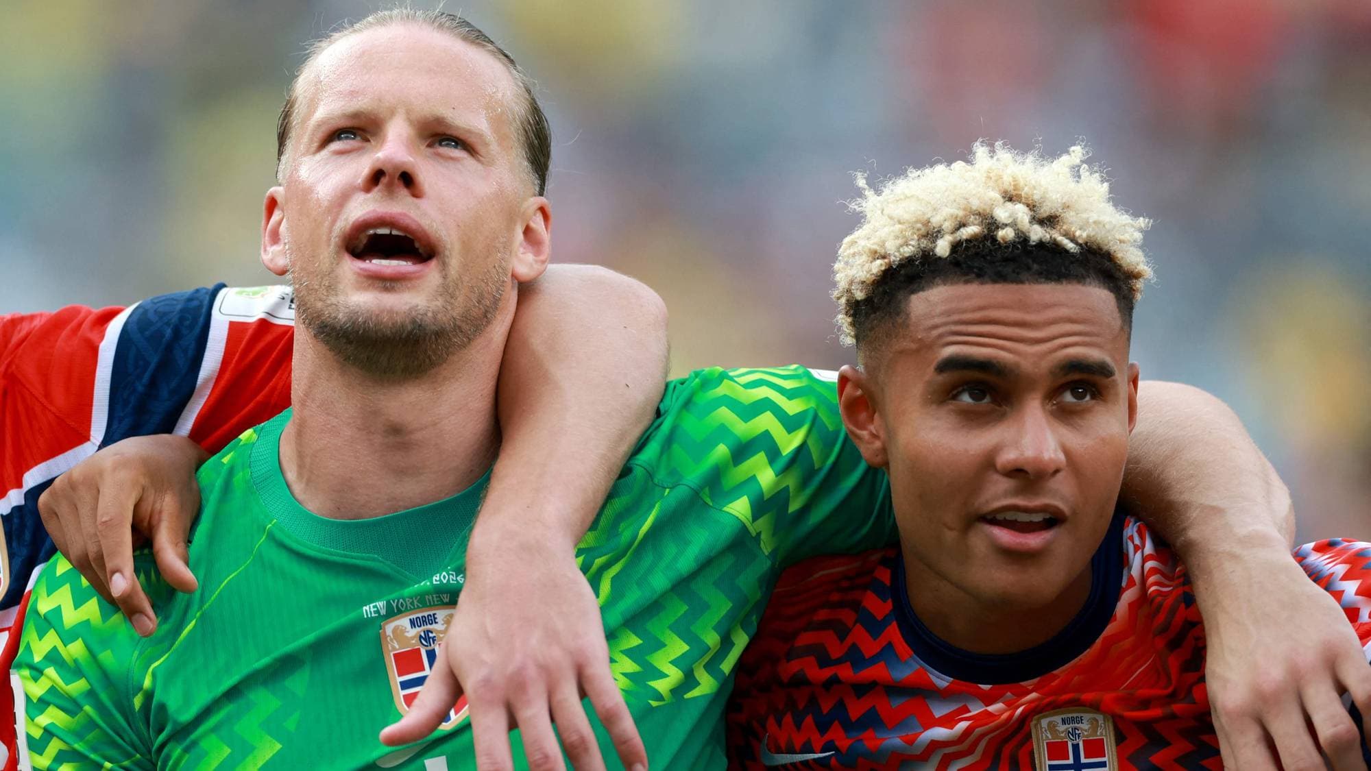 Tre norske fotballspillere med armene rundt hverandre på banen under en landskamp. (Bildebeskrivelsen er laget av en KI-tjeneste)