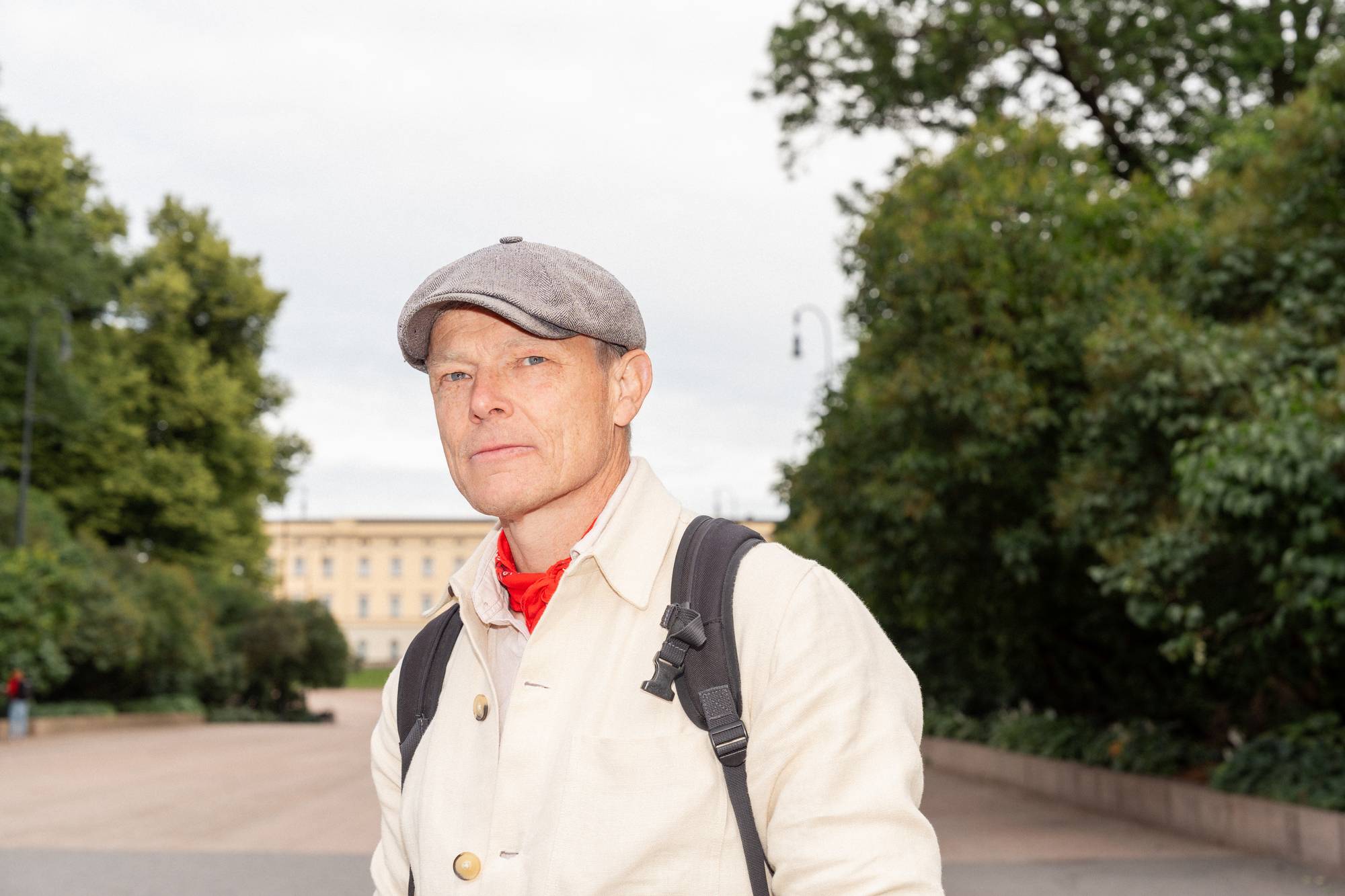 Mann med caps, lyst tøy og ryggsekk foran Slottet i Oslo. (Bildebeskrivelsen er laget av en KI-tjeneste)
