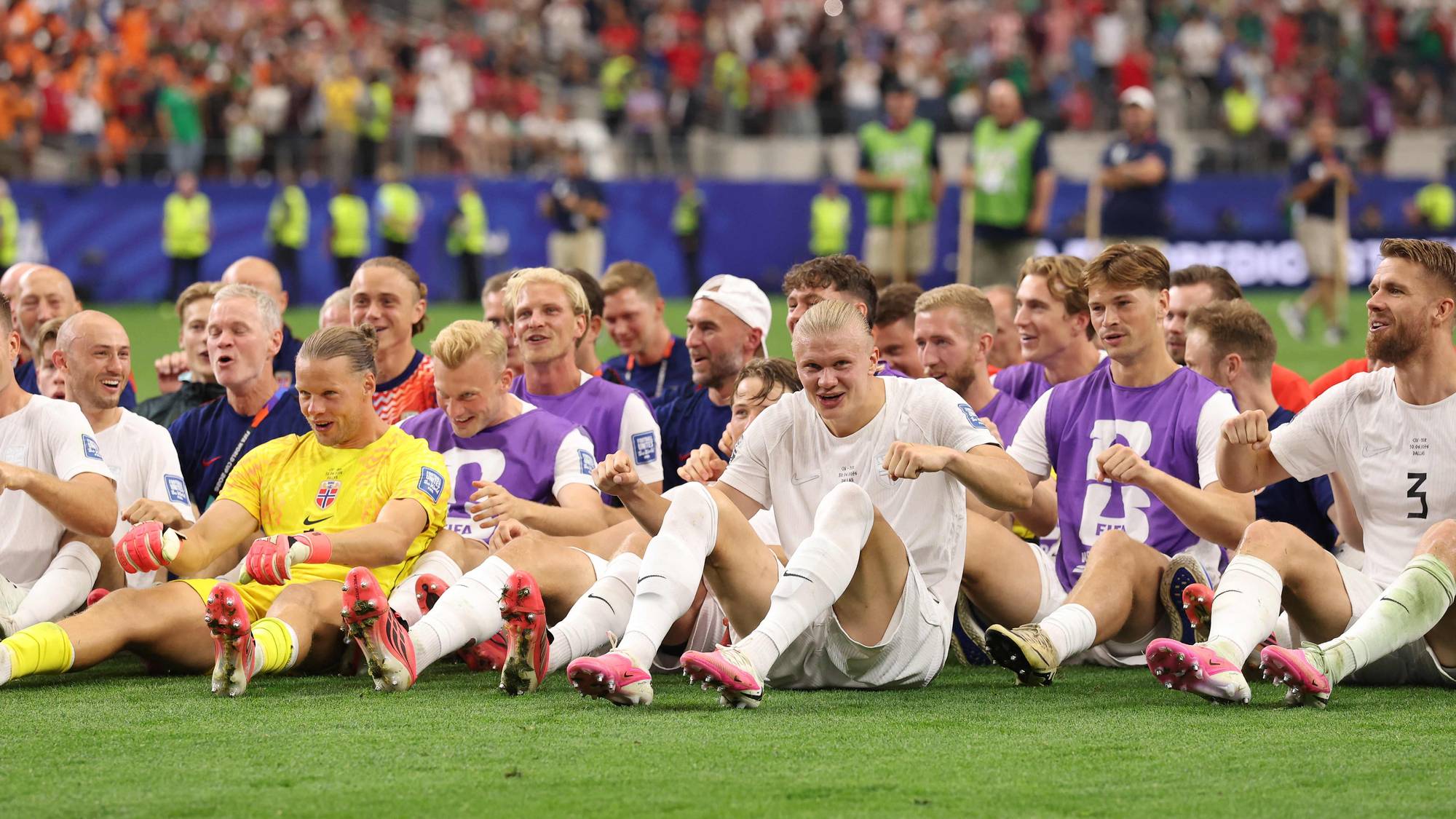 Norske fotballspillere sitter på gresset etter en kamp på en fullsatt stadion. (Bildebeskrivelsen er laget av en KI-tjeneste)
