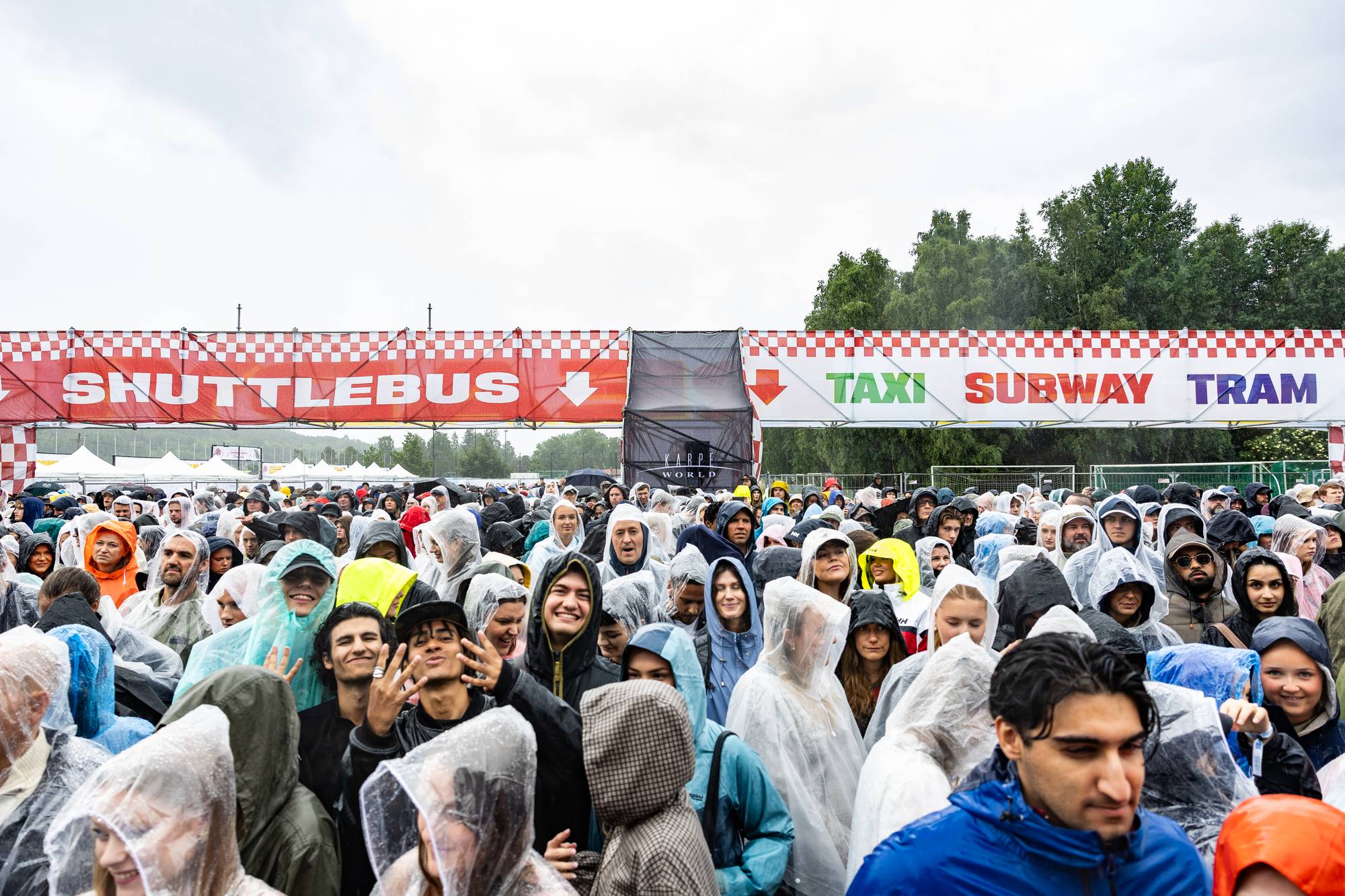 Menneskemengde i regntøy under et skilt for kollektivtransport ved en Karpe-konsert. (Bildebeskrivelsen er laget av en KI-tjeneste)