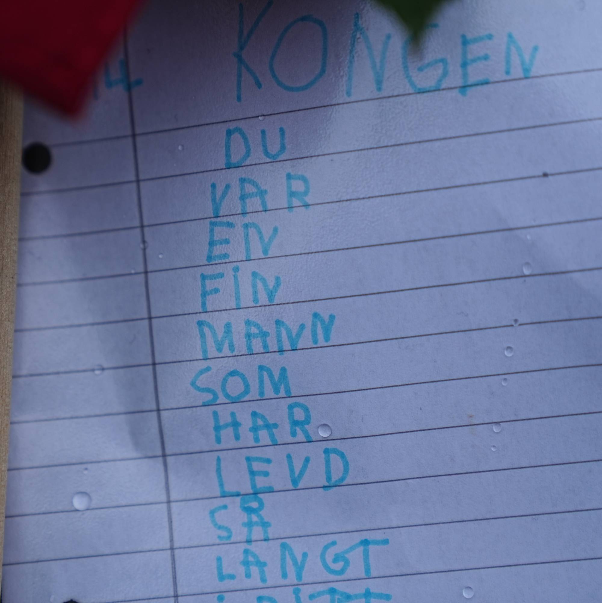 Håndskrevet hilsen med blå tekst på et ark med linjer, adressert til kongen.