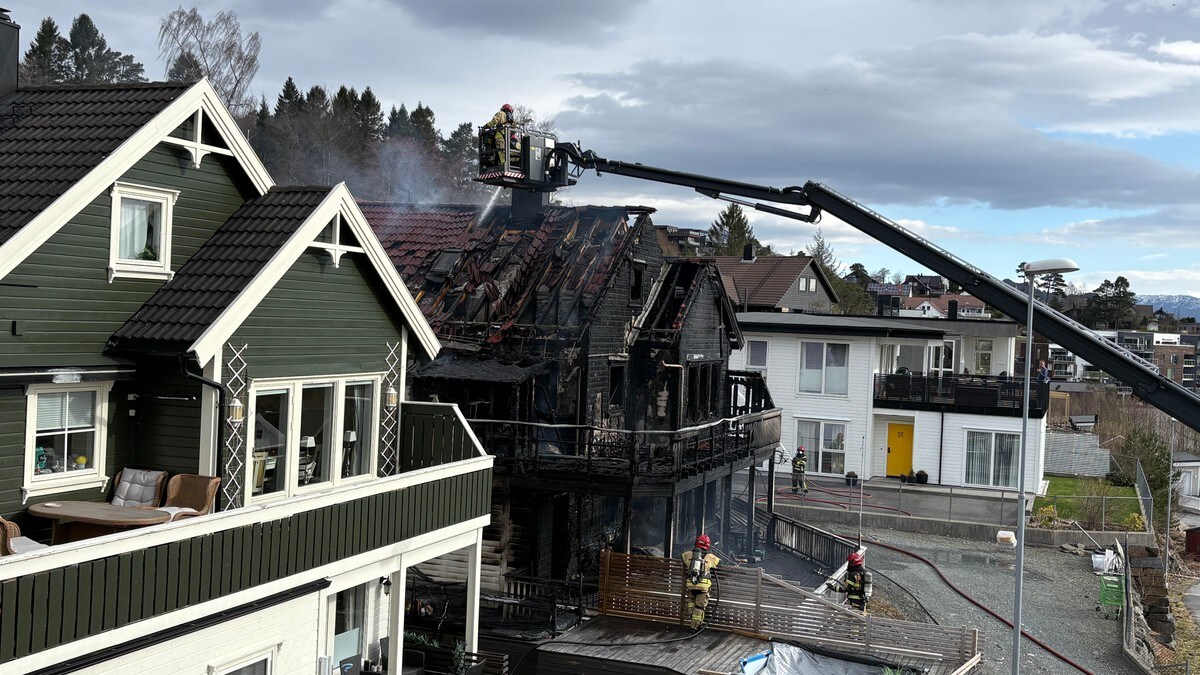 Brannmannskaper jobber med restene av et utbrent hus. Et brannmannskap befinner seg i en lift og sprøyter vann på taket av huset. Flere brannmenn er samlet rundt huset og holder i brannslanger. Det er røyk som stiger fra det ødelagte huset. FOTO: Arne Frank Solheim/NRK