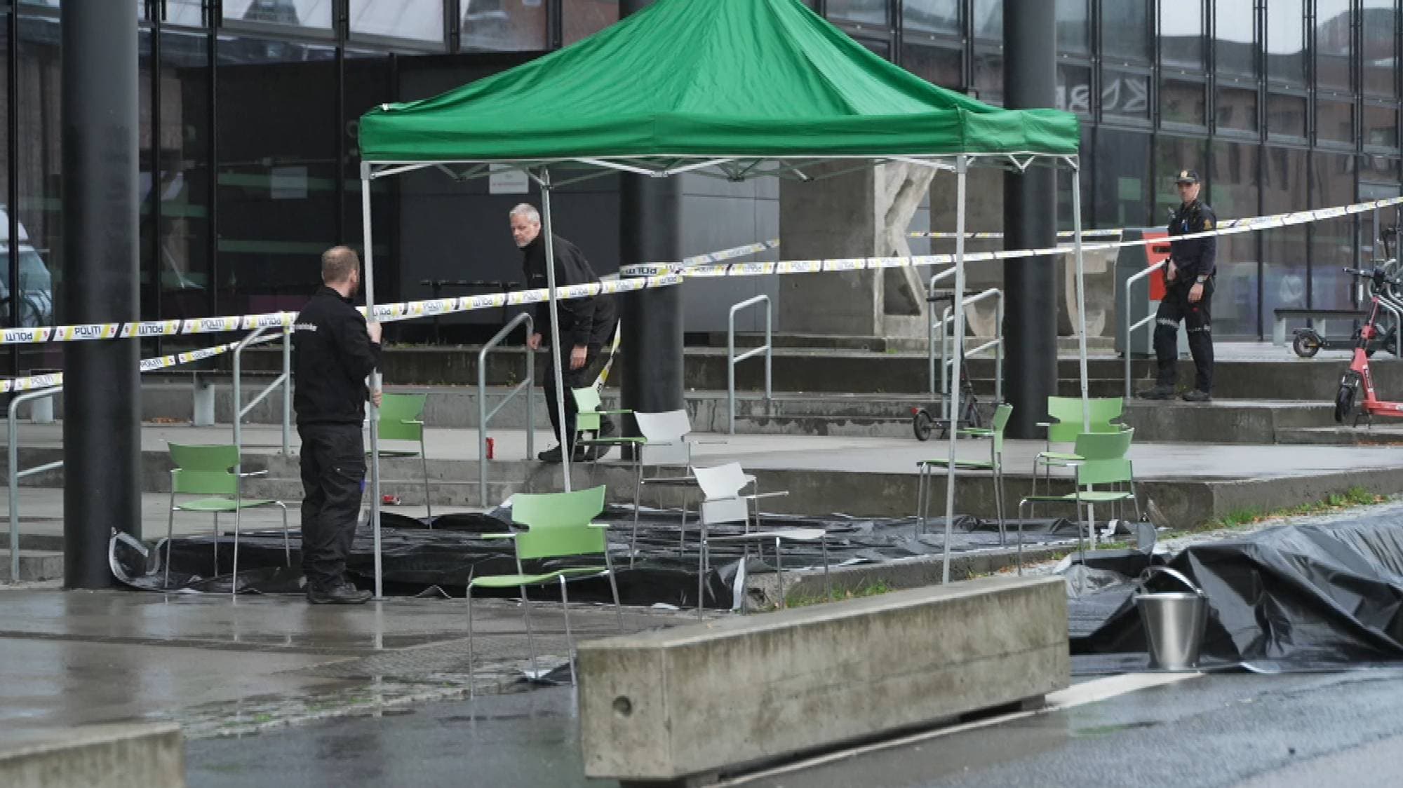 Politiet undersøker et område avsperret med politibånd ved et grønt telt utenfor en bygning. (Bildebeskrivelsen er laget av en KI-tjeneste)