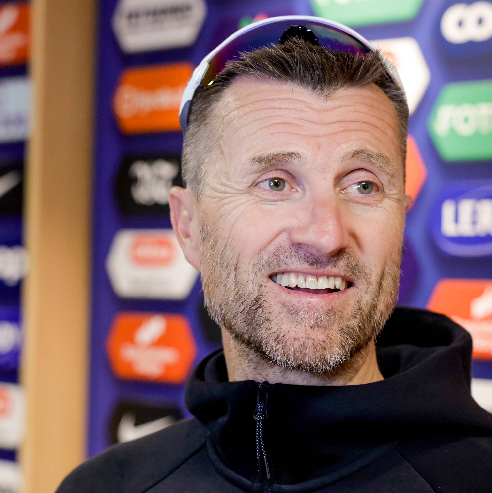 Eirik Horneland smiler foran en vegg med sponsorlogoer. 