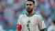 Mosa'ab Elshamy / AP,NTB Fotballspiller i hvit drakt med grønne detaljer og algerisk emblemer. Spilleren har et rødt armbånd. Bakgrunnen viser et utydelig publikum. Bildet er et fotografi. (Bildebeskrivelsen er laget av en KI-tjeneste)