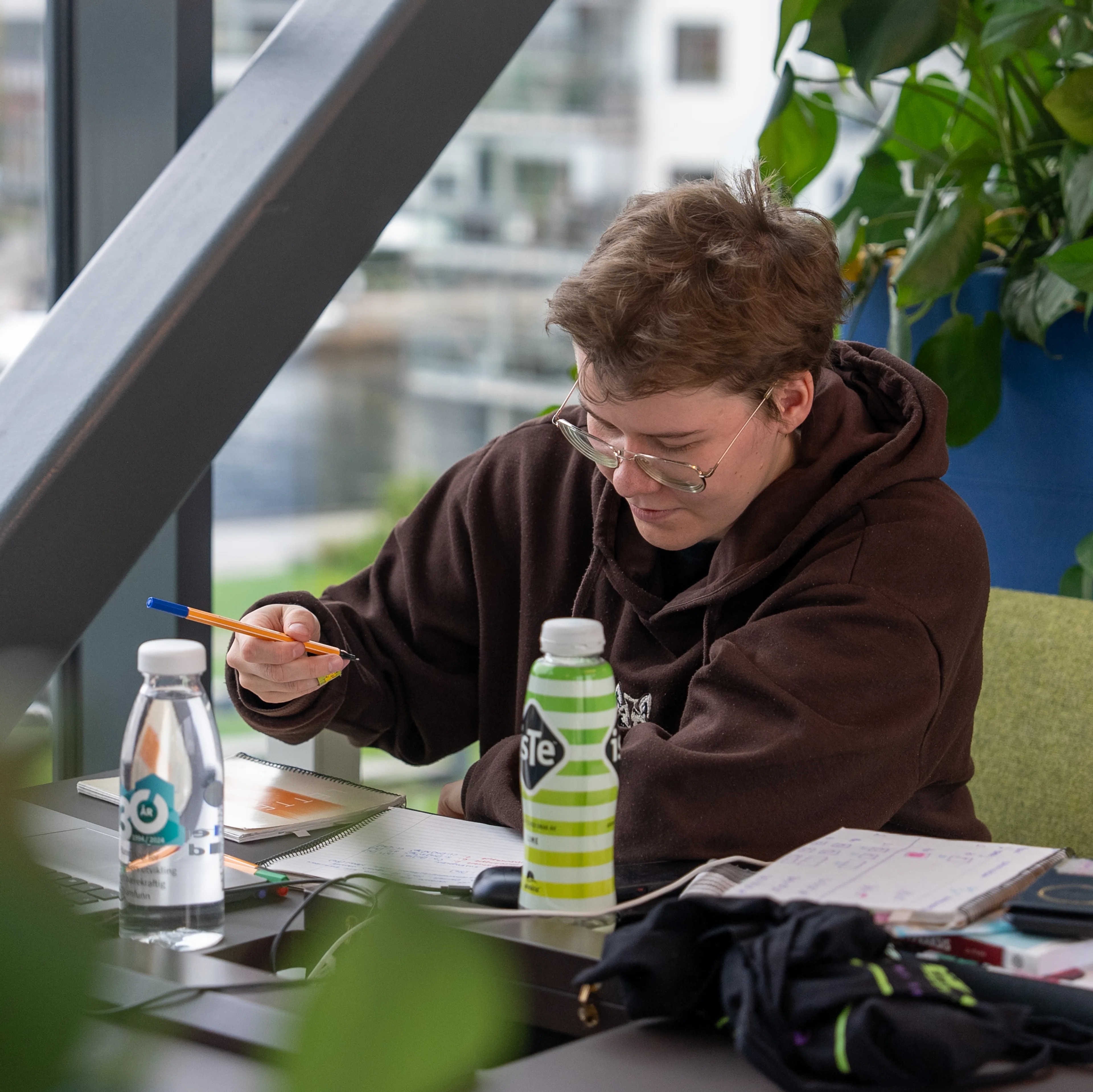 Person sitter ved et bord og skriver i en notatbok ved et vindu. (Bildebeskrivelsen er laget av en KI-tjeneste)
