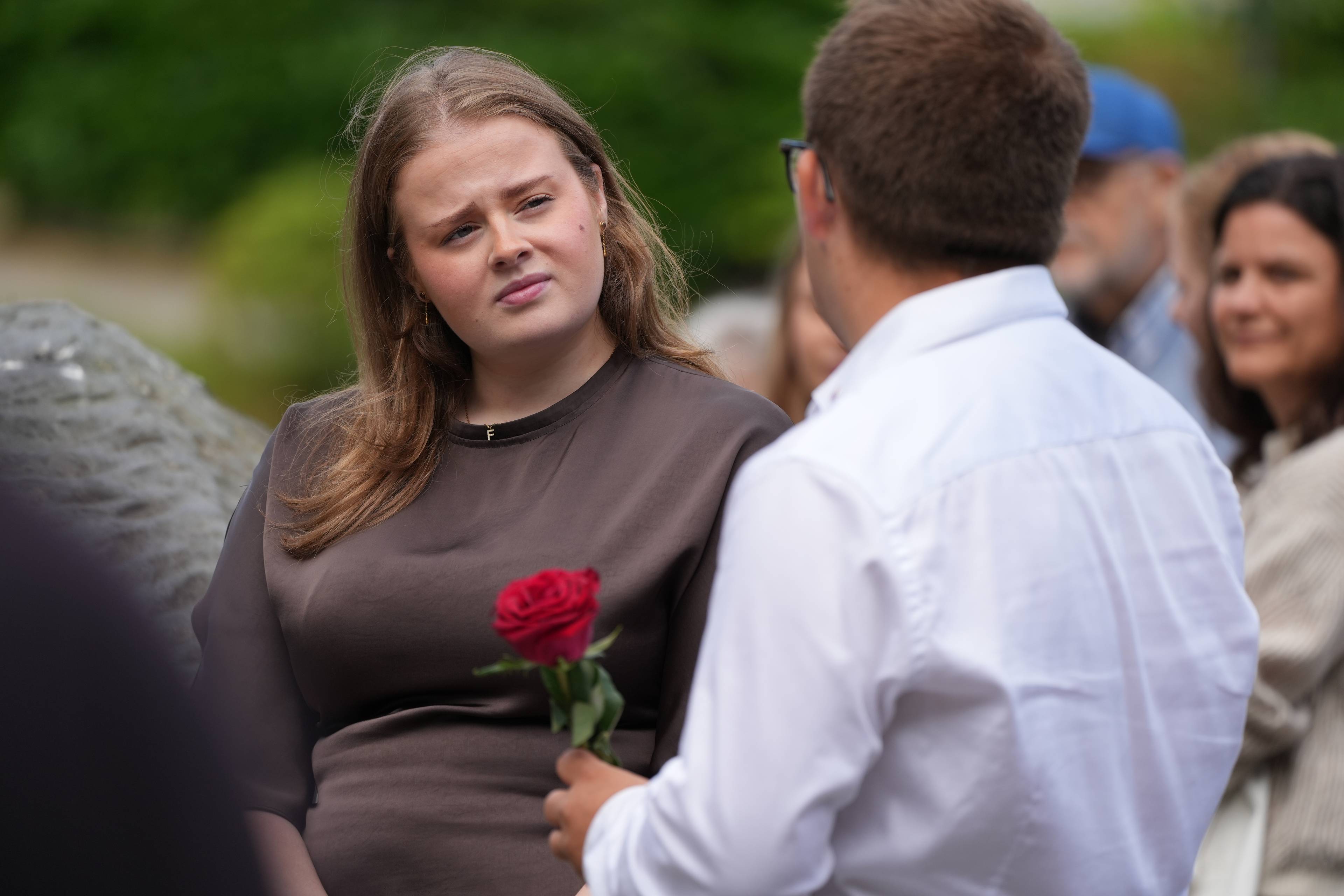 Kvinne ser på en mann som holder en rød rose i et utendørs miljø. (Bildebeskrivelsen er laget av en KI-tjeneste)
