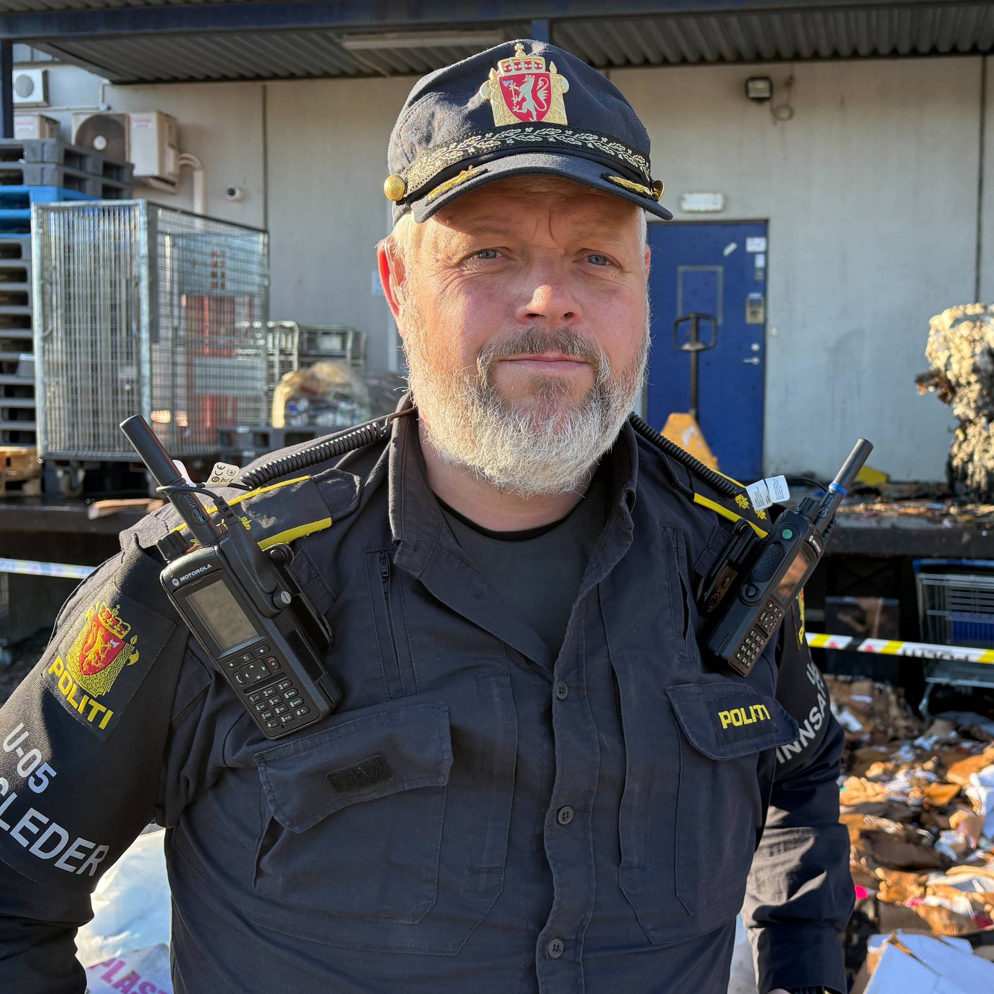 En mann i politiuniform står foran et område som er sperret av i forbindelse med en brann.
