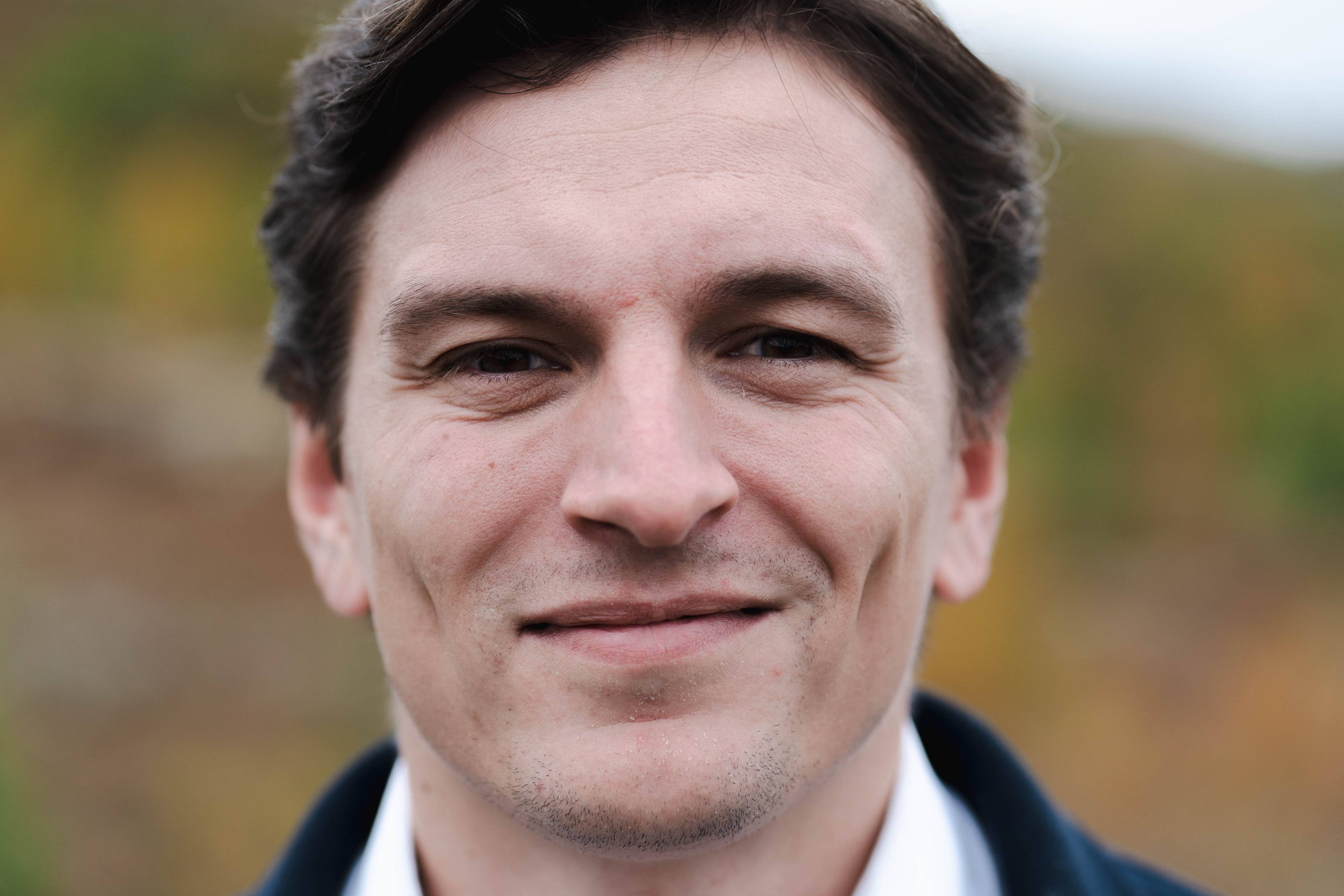 Portrett av en mann med mørkt hår, sett forfra mot en utydelig bakgrunn. (Bildebeskrivelsen er laget av en KI-tjeneste)
