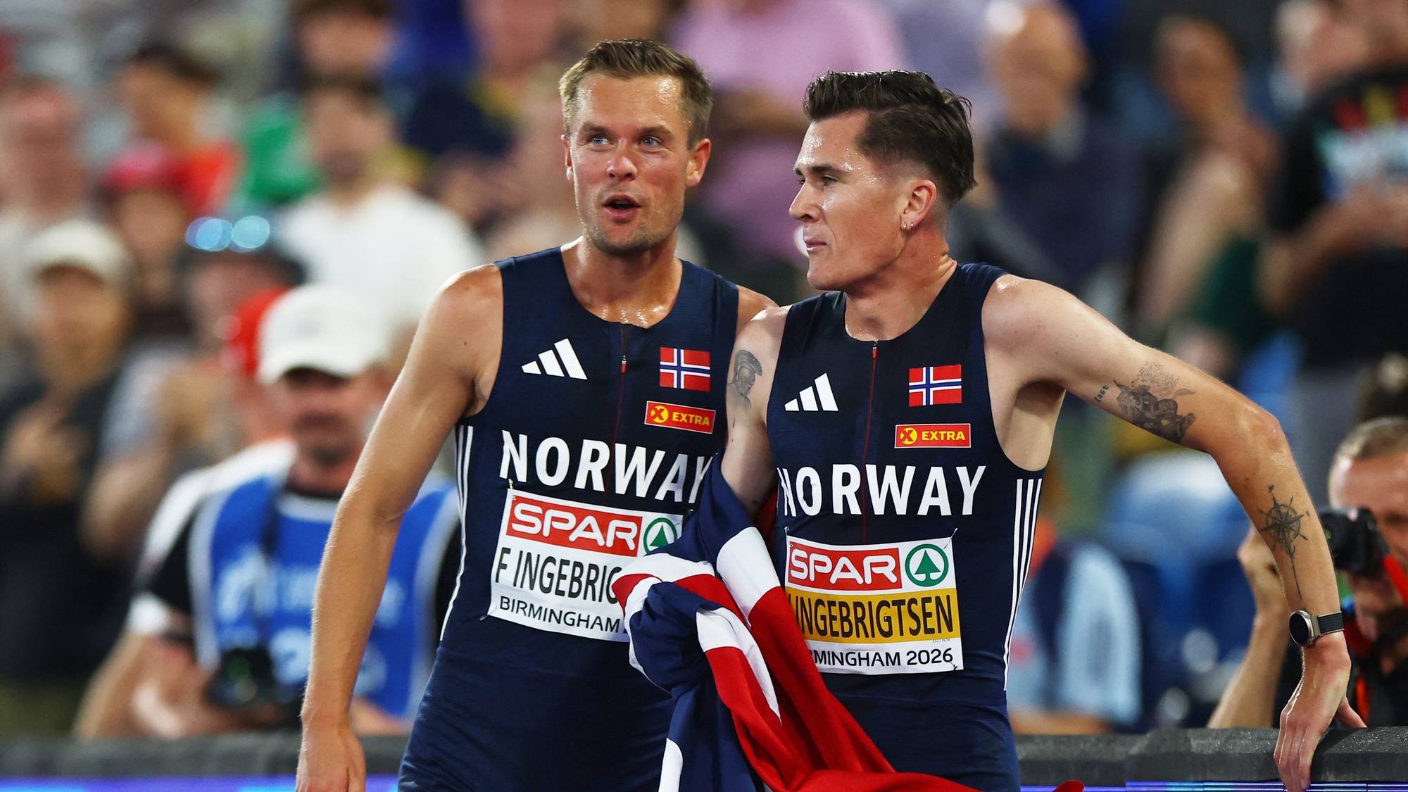 Filip og Jakob Ingebrigtsen feirer med norsk flagg etter et friidrettsløp på stadion. (Bildebeskrivelsen er laget av en KI-tjeneste)