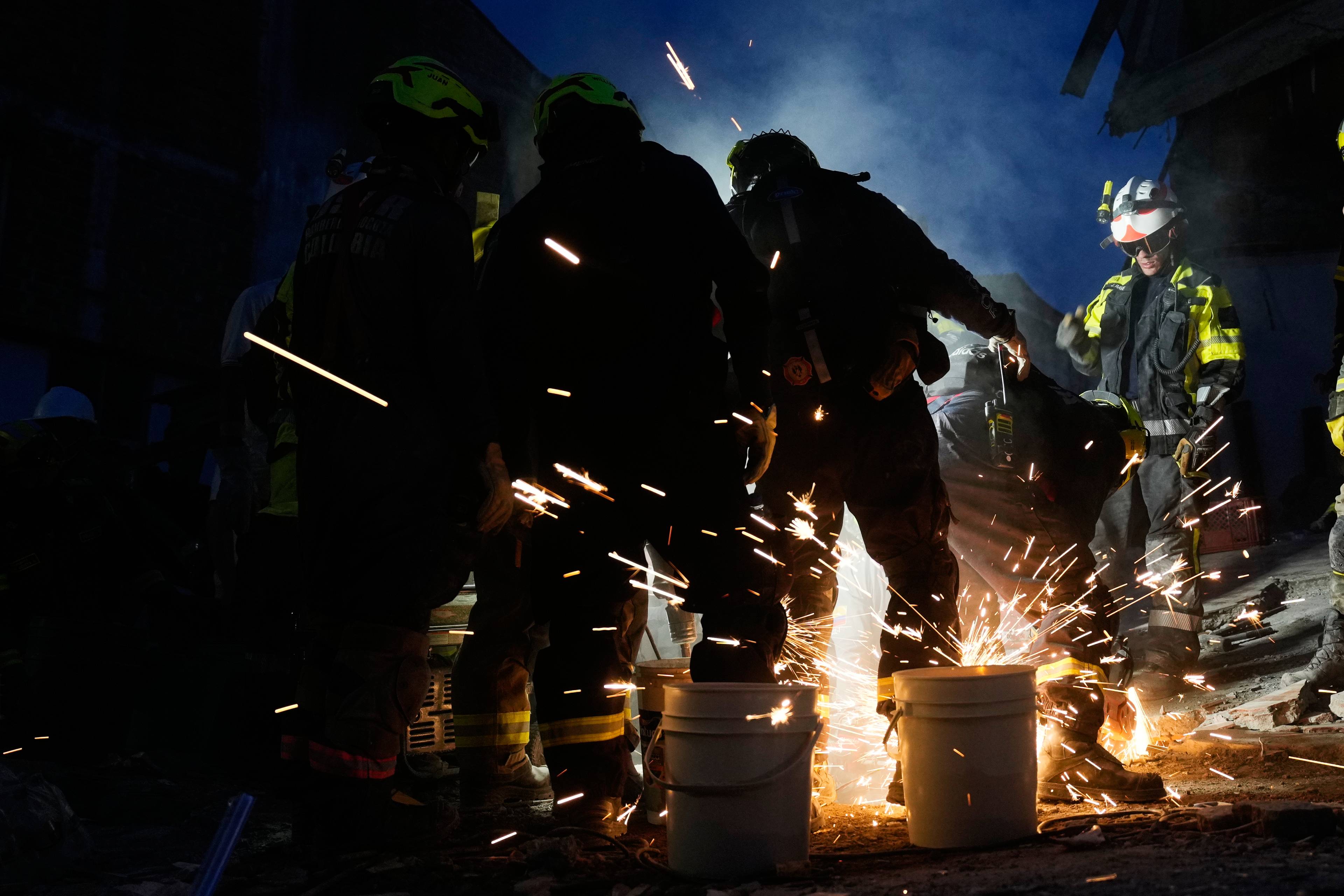 Redningsmannskaper bruker skjærebrenner i mørket, med gnister som spruter ut. (Bildebeskrivelsen er laget av en KI-tjeneste)