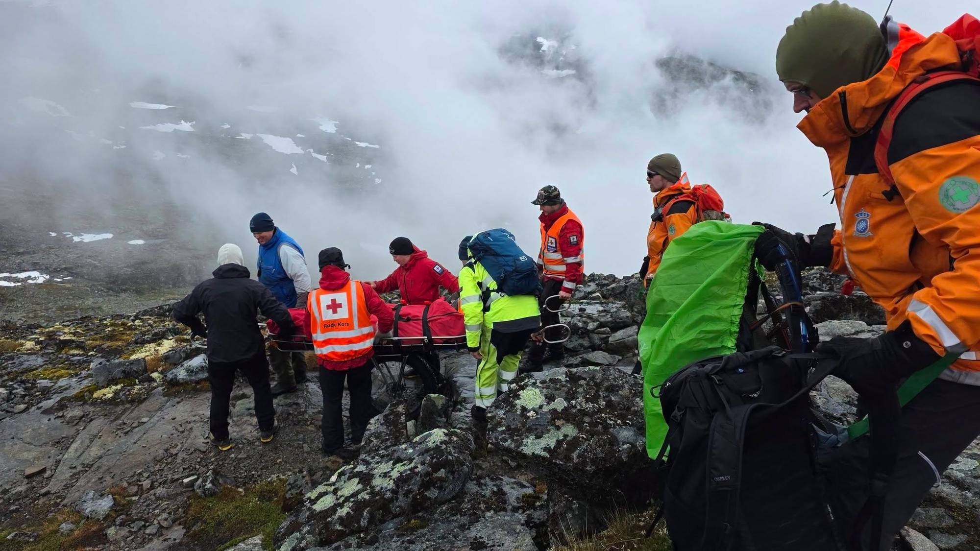 Redningsmannskap som går ned eit fjell med ein person i båre. 