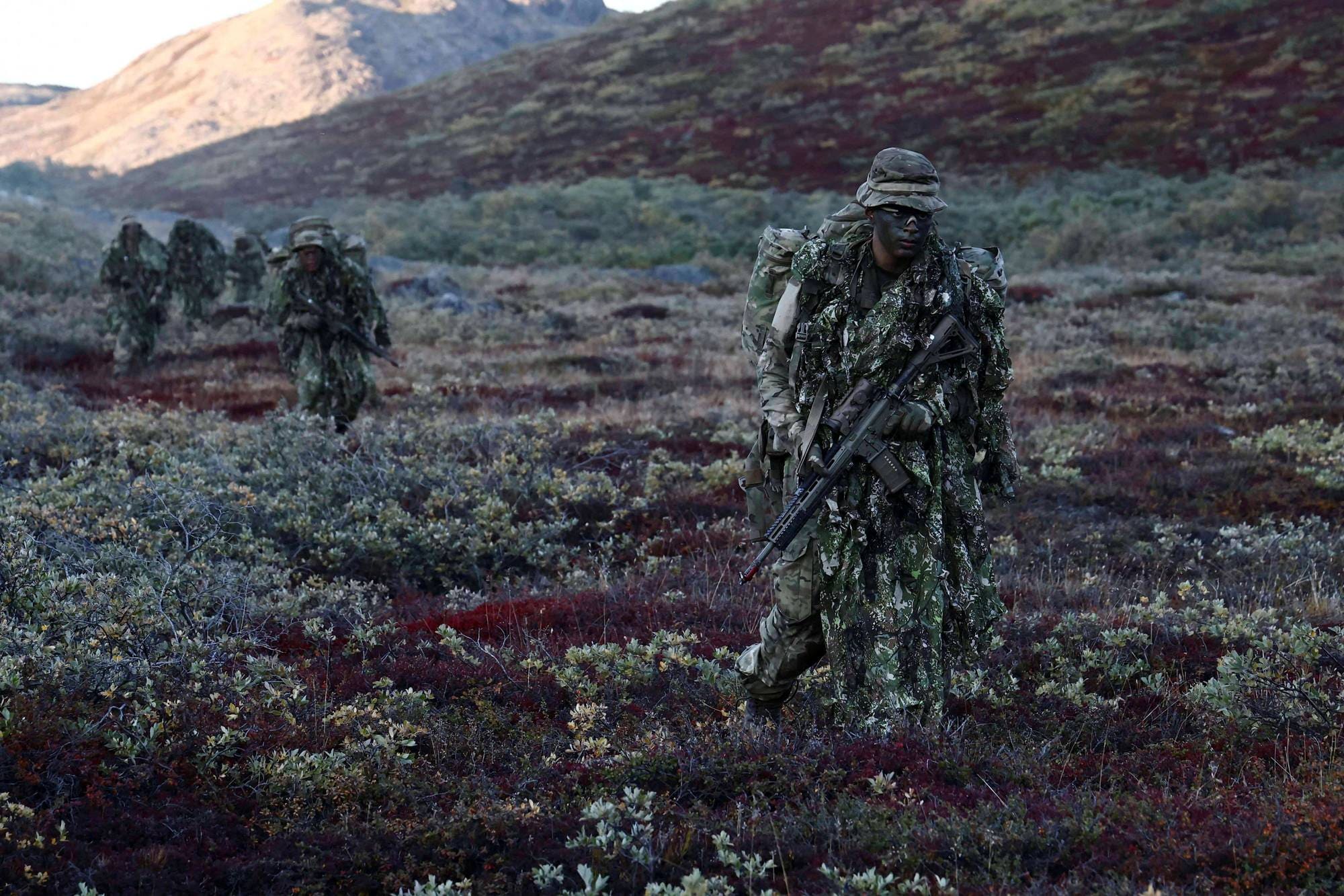 Soldater i kamuflasjeutstyr går gjennom et fjellandskap i høstfarger. (Bildebeskrivelsen er laget av en KI-tjeneste)