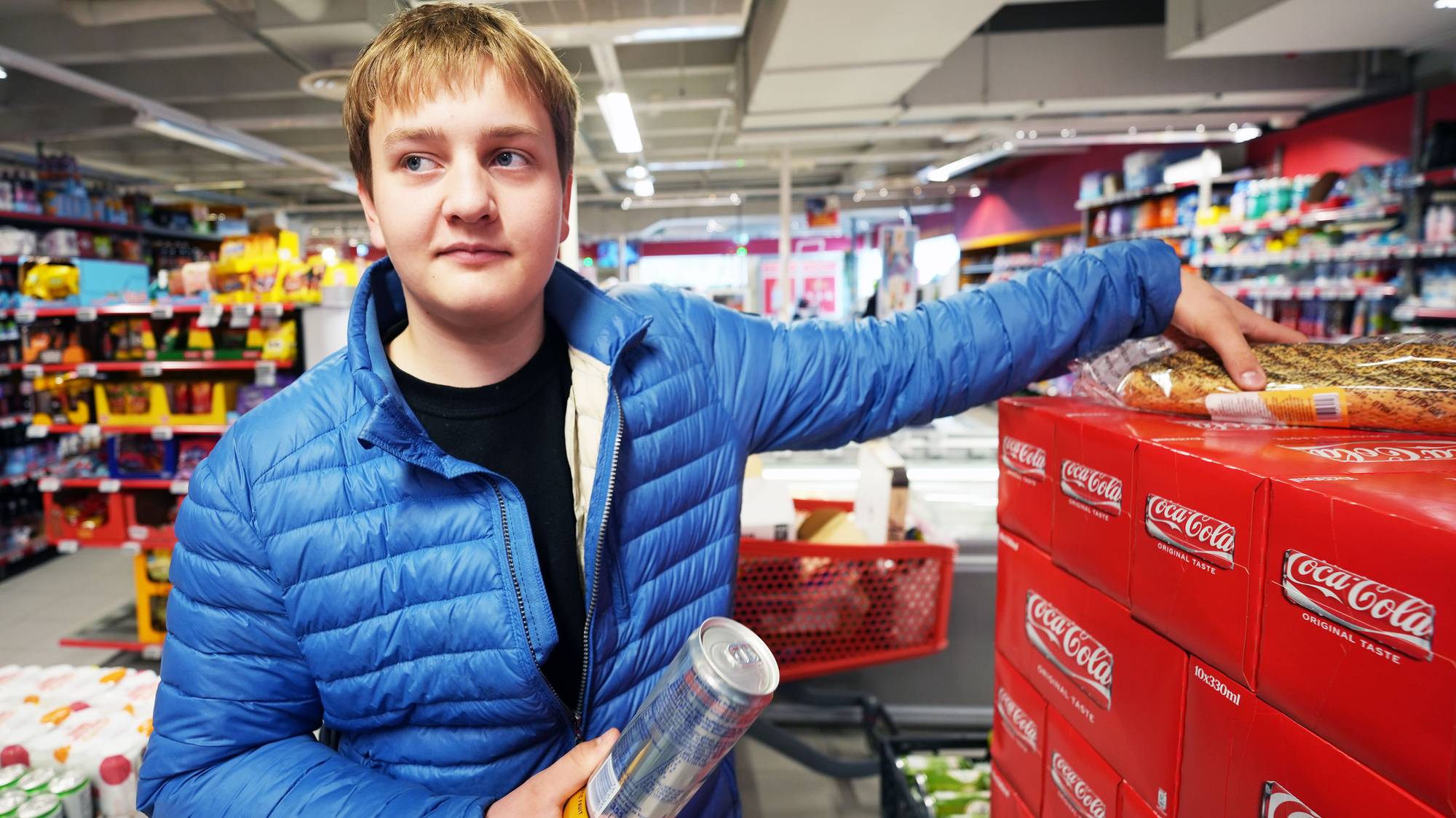 En mann i blå jakke står i en dagligvarebutikk og holder en vare ved en pallesalgsenhet. (Bildebeskrivelsen er laget av en KI-tjeneste)