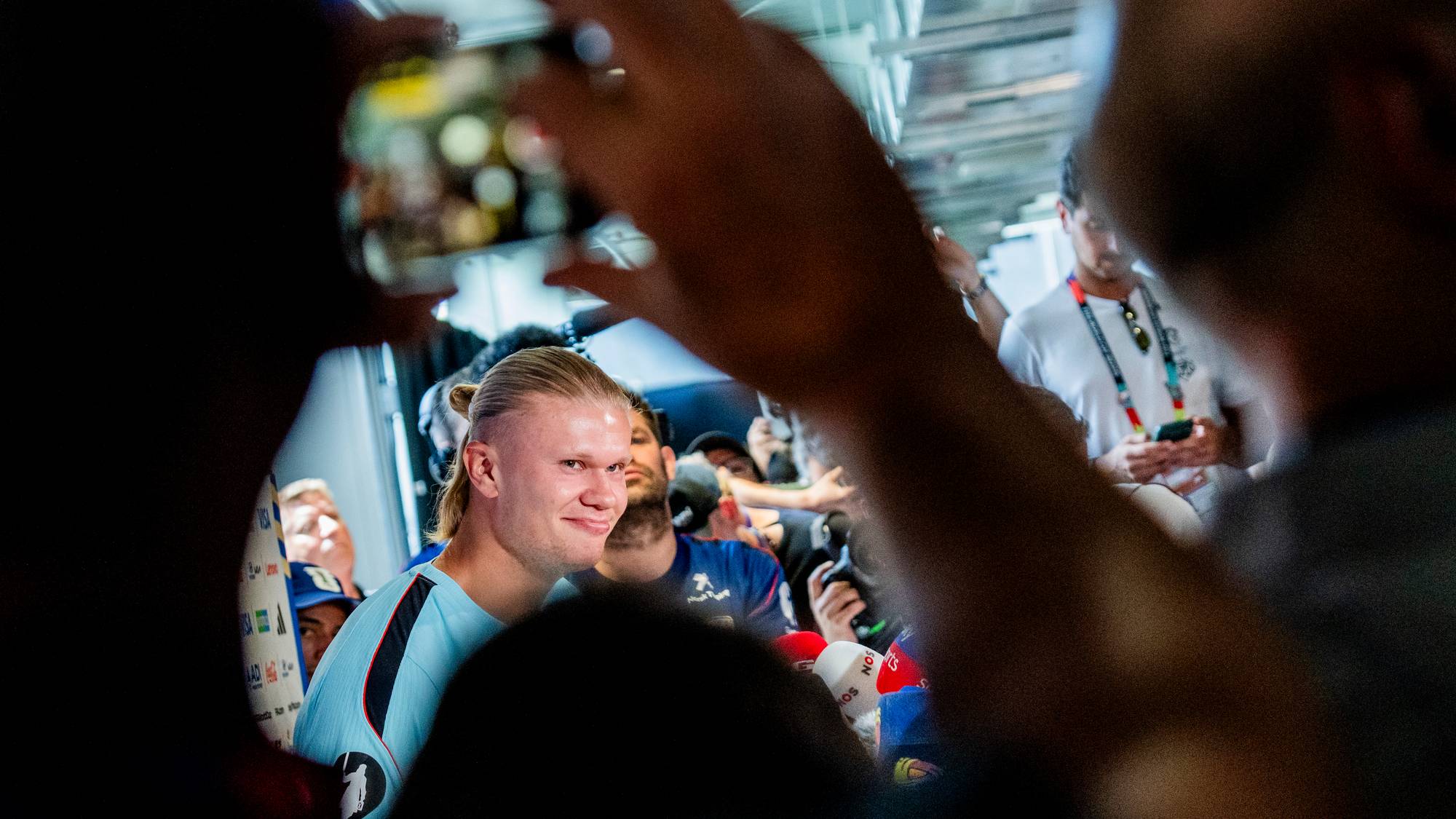 Erling Braut Haaland omgitt av pressefolk som tar bilder med mobiltelefoner og mikrofoner. (Bildebeskrivelsen er laget av en KI-tjeneste)