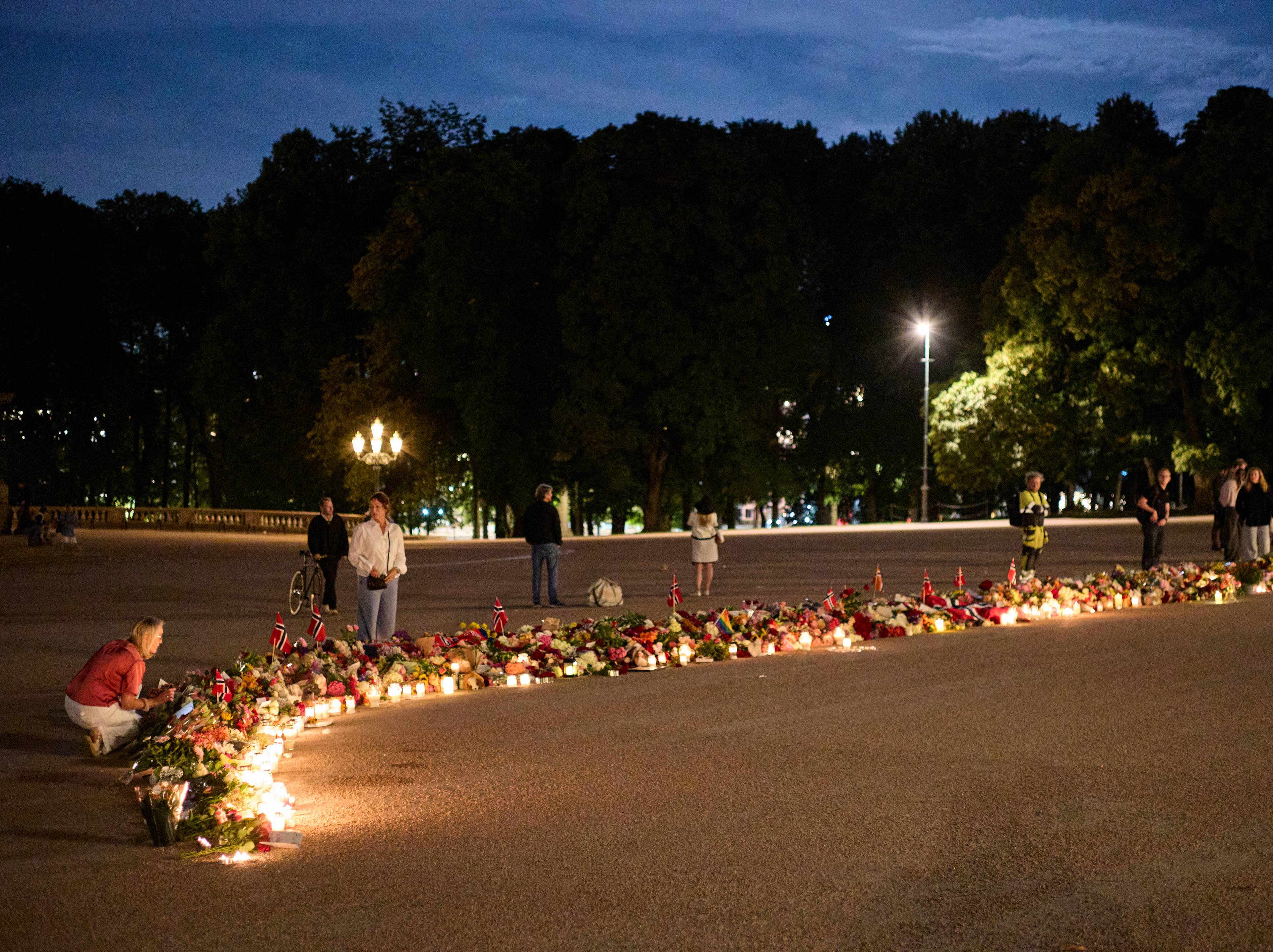 Folk legger ned blomster og tenner lys foran Slottet i Oslo på kveldstid.