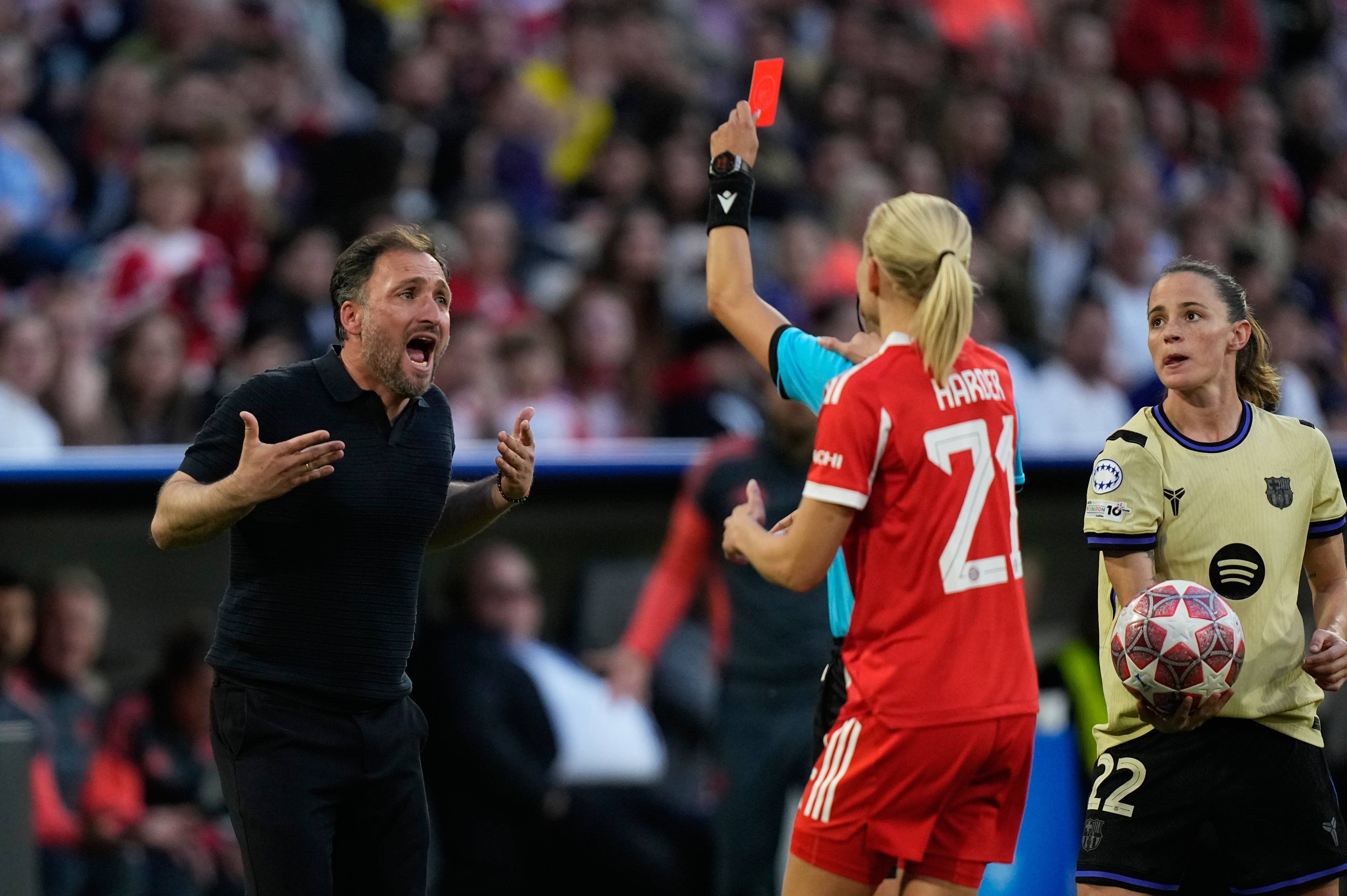 En dommer holder opp et rødt kort. En fotballtrener reagerer med gestikulering, mens en spiller med en fotball står til høyre. Det er publikum i bakgrunnen. (Bildebeskrivelsen er laget av en KI-tjeneste)