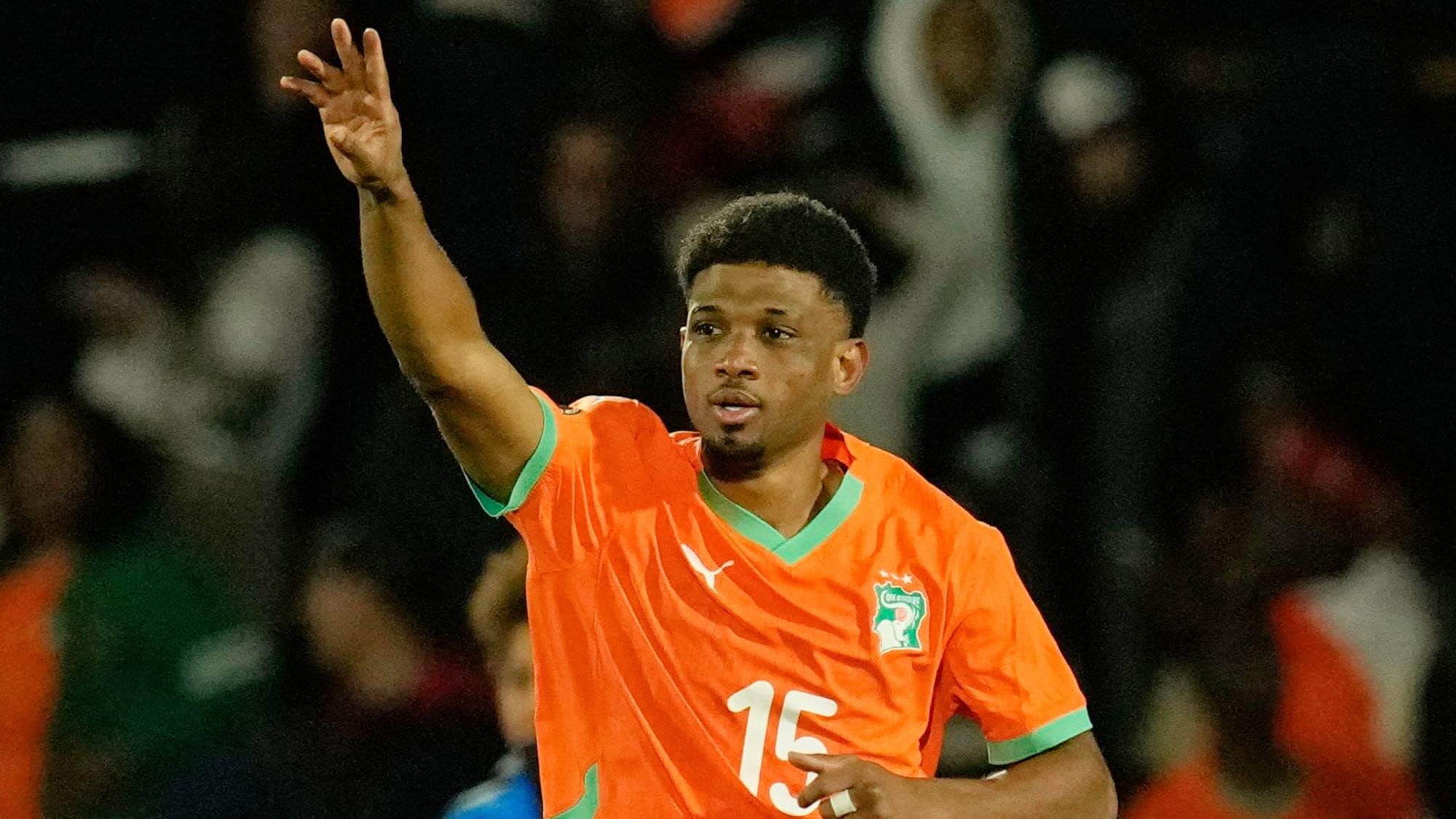 Fotballspiller i oransje drakt med nummer 15 vinker med hånden. Spilleren er fra Elfenbenskysten. Bakgrunnen er mørk og viser tilskuere. (Bildebeskrivelsen er laget av en KI-tjeneste)