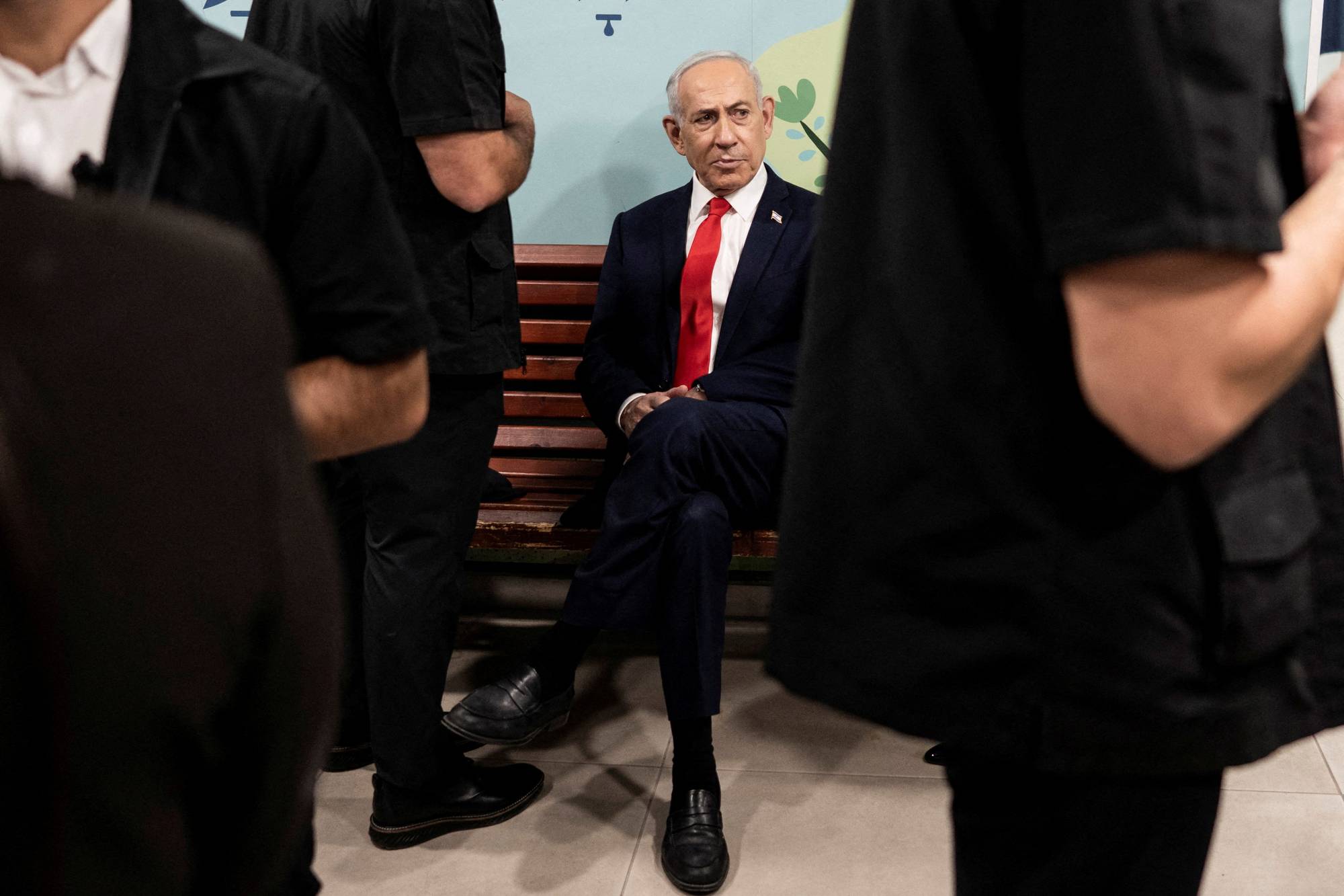 Israels statsminister Benjamin Netanyahu sitter på en benk omgitt av vakter. (Bildebeskrivelsen er laget av en KI-tjeneste)