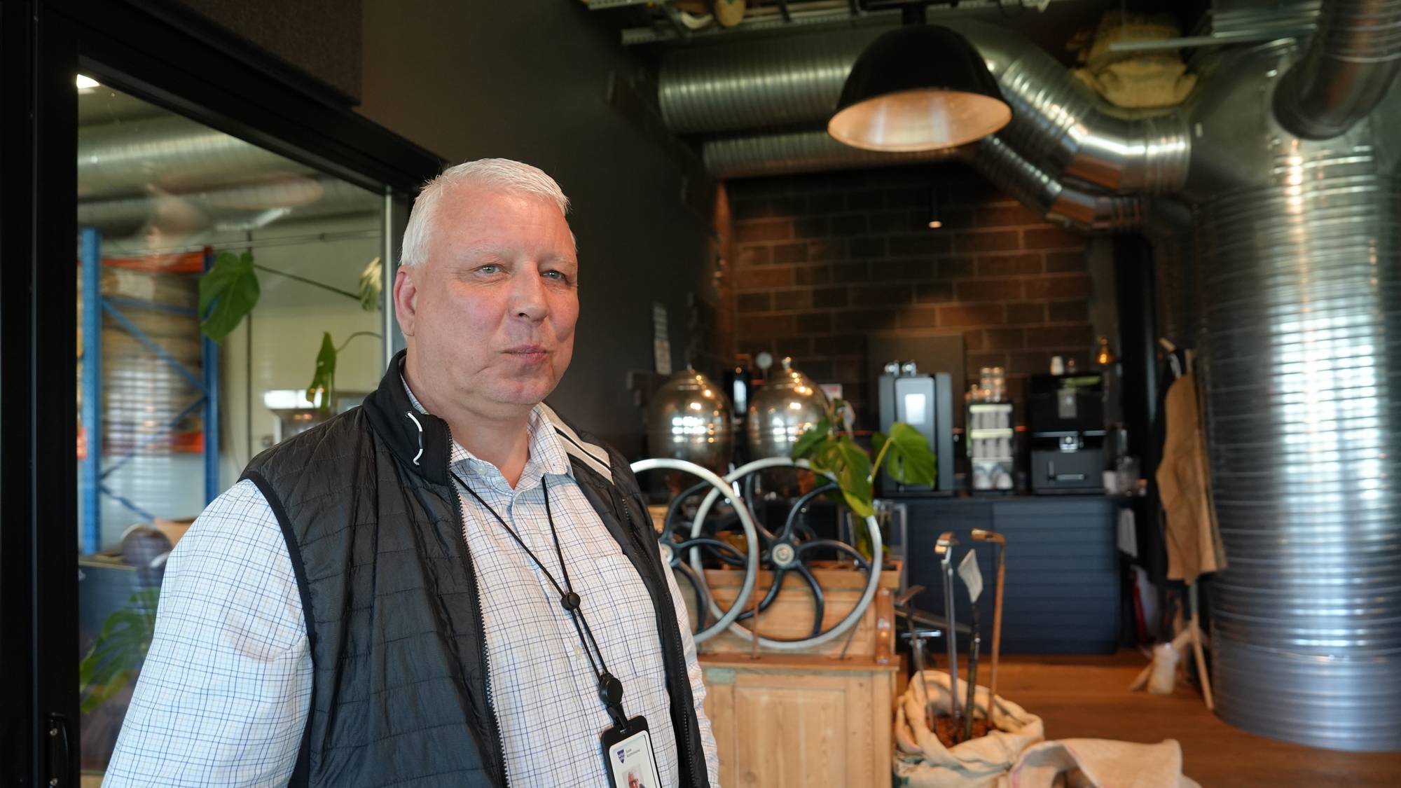 Mann med vest og skjorte. Mannen står inne i en kaffebutikk. 