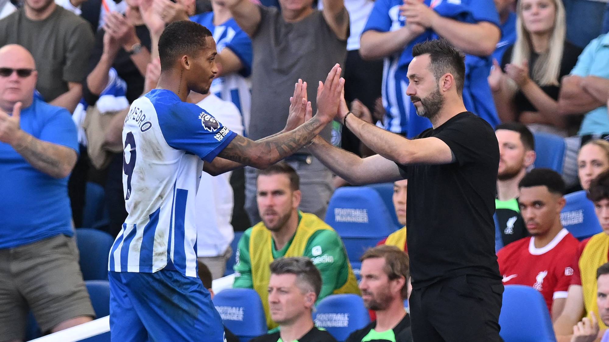 Fotballspilleren João Pedro gir en high-five til treneren sin ved sidelinjen under en kamp. (Bildebeskrivelsen er laget av en KI-tjeneste)