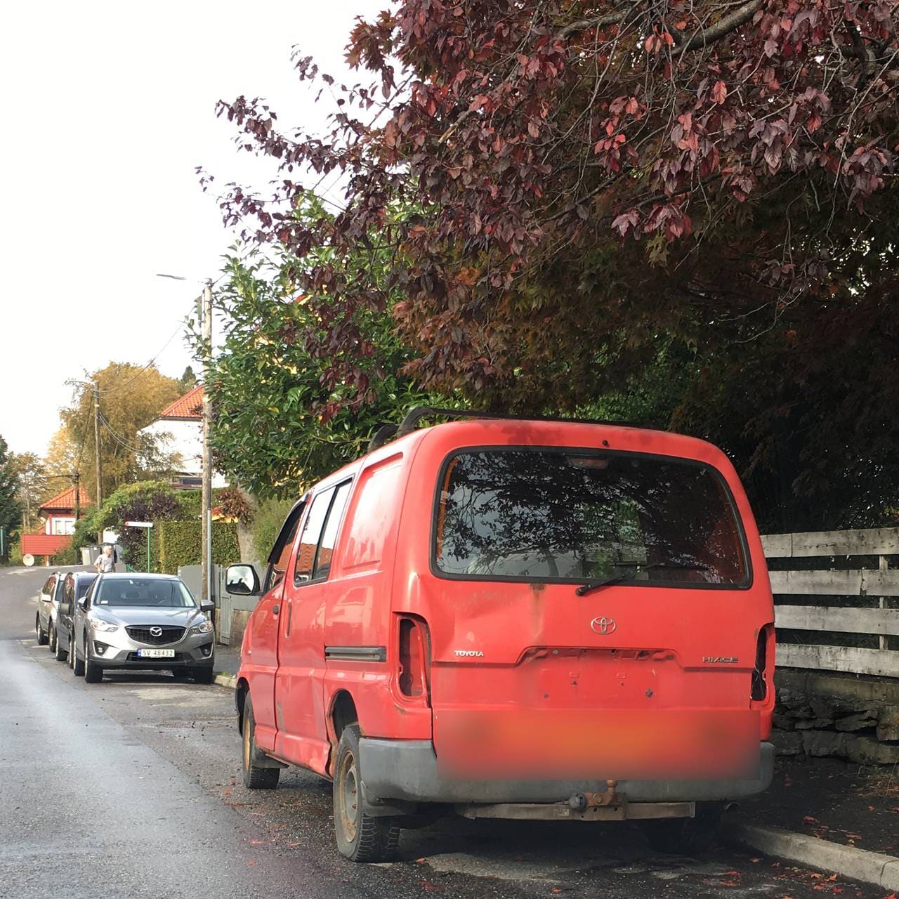 En rød bil uten skilt står parkert i et boligstrøk