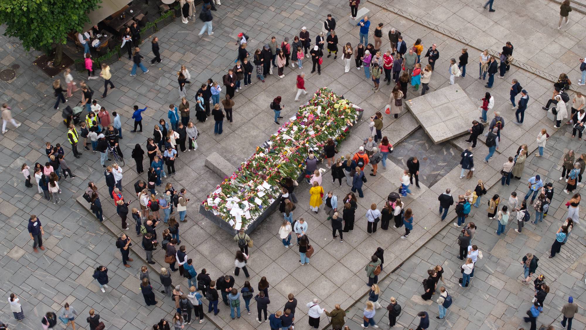 oversiktsbilde der ein ser mange menneske rundt den blå stein, der det ligg blomar