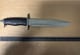Politiet Et stort kniv med svart håndtak og et langt, bredt blad ligger på en brun overflate. Kniven har en taggete del på oversiden av bladet. En målestokk ligger under kniven, som viser centimeter opp til 37. (Bildebeskrivelsen er laget av en KI-tjeneste)