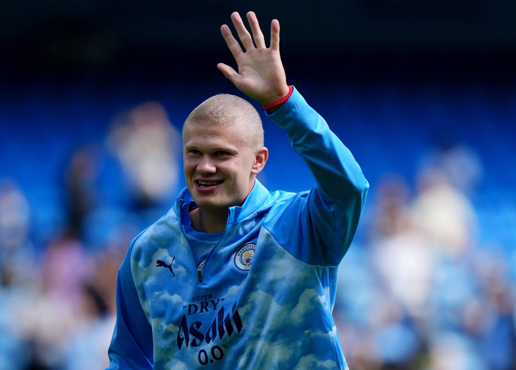 Erling Braut Haaland vinker til publikum ikledd Manchester City-treningstøy på en fotballarena. (Bildebeskrivelsen er laget av en KI-tjeneste)