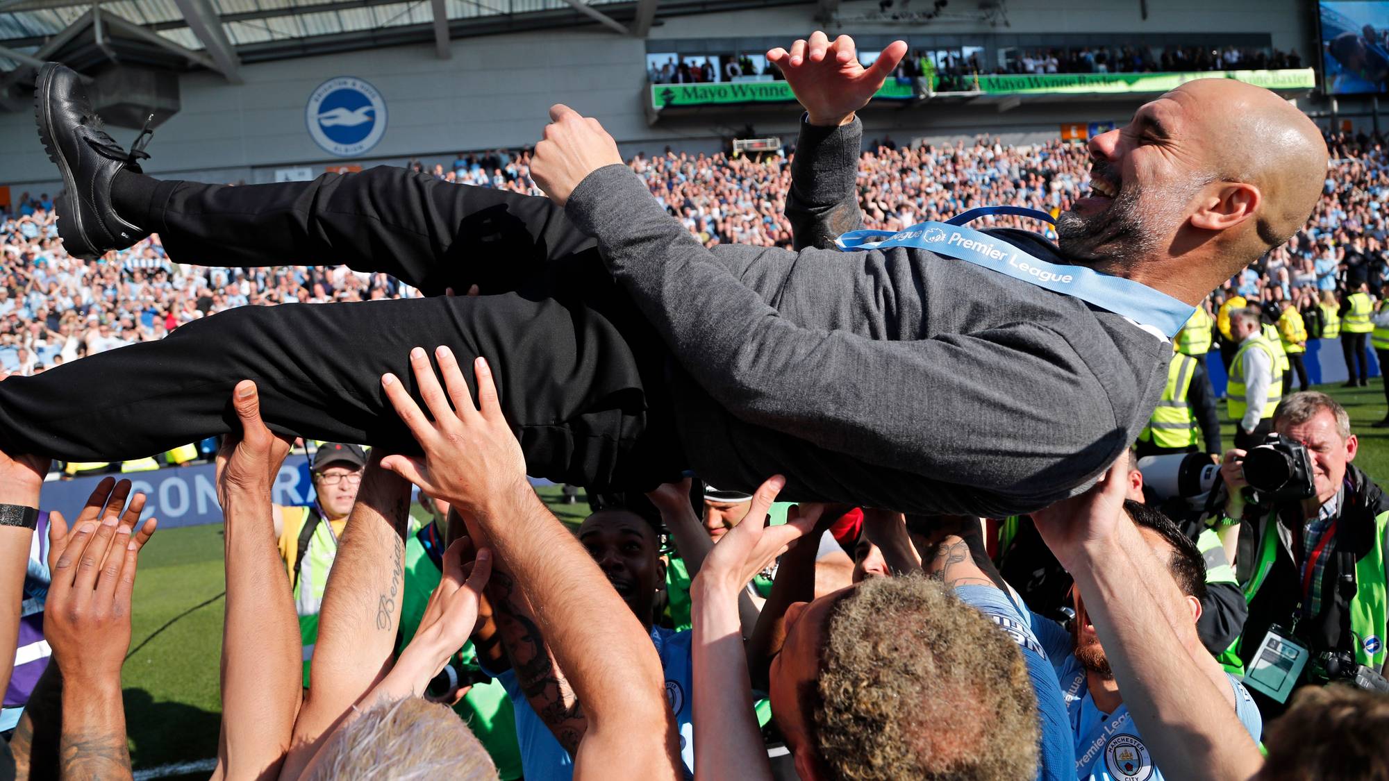 Pep Guardiola løftes opp av spillerne sine på en fotballstadion etter seier. (Bildebeskrivelsen er laget av en KI-tjeneste)