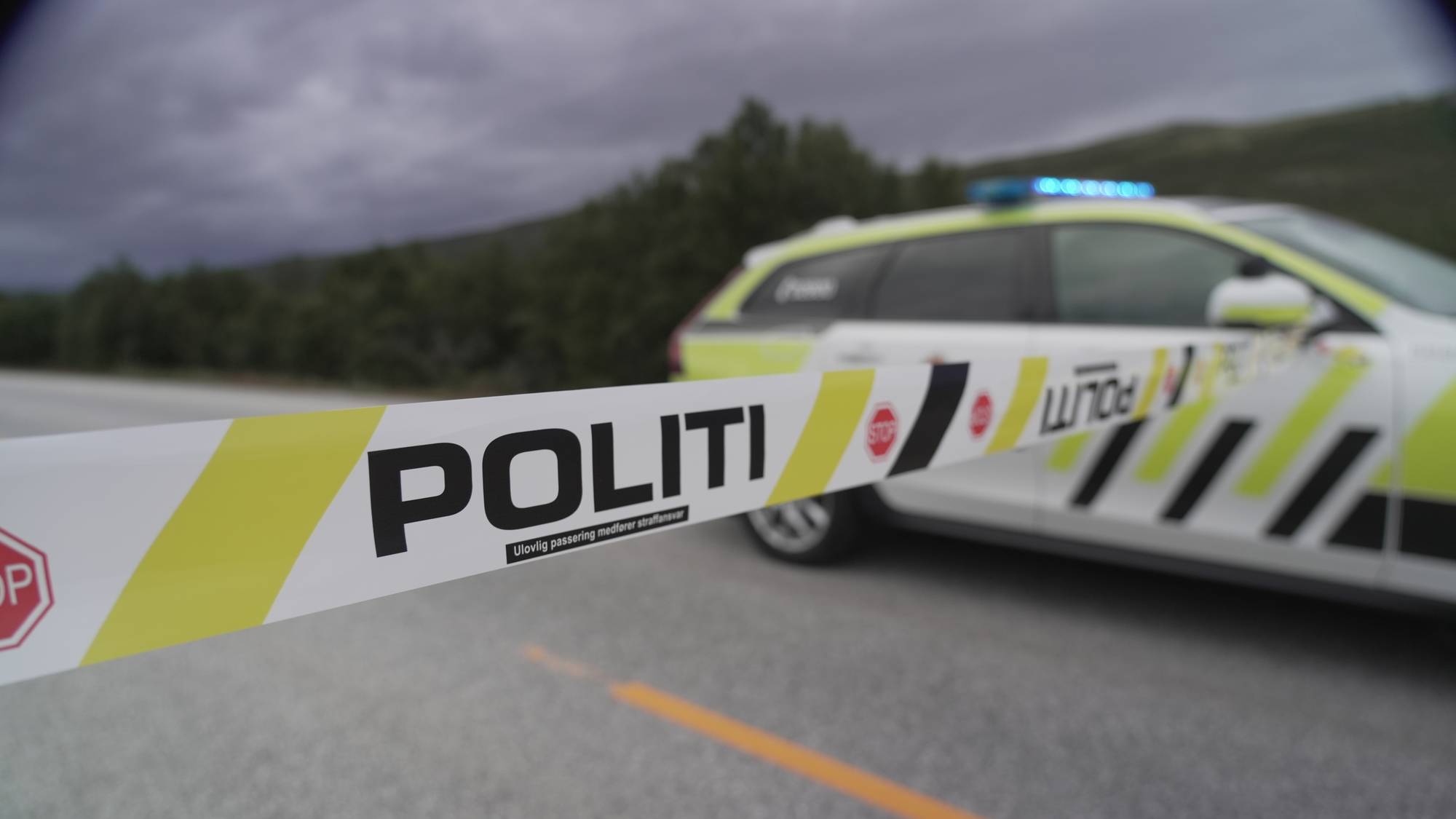 Politisperrebånd foran en politibil på en vei.