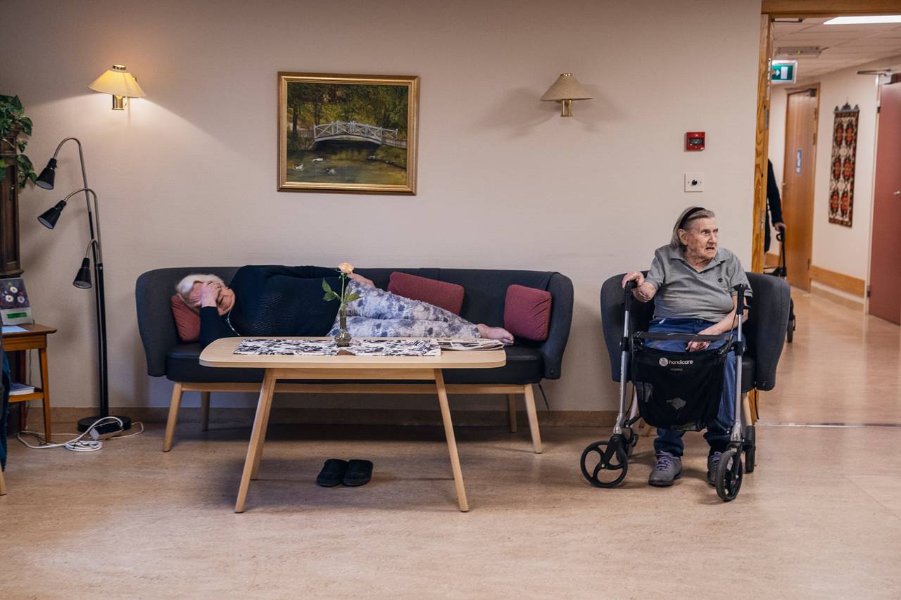 Anne Marie har lagt seg langflat på sofaen med hånden foran øynene. Ved siden av sitter Eugenie i en stol med rullatoren sin foran.