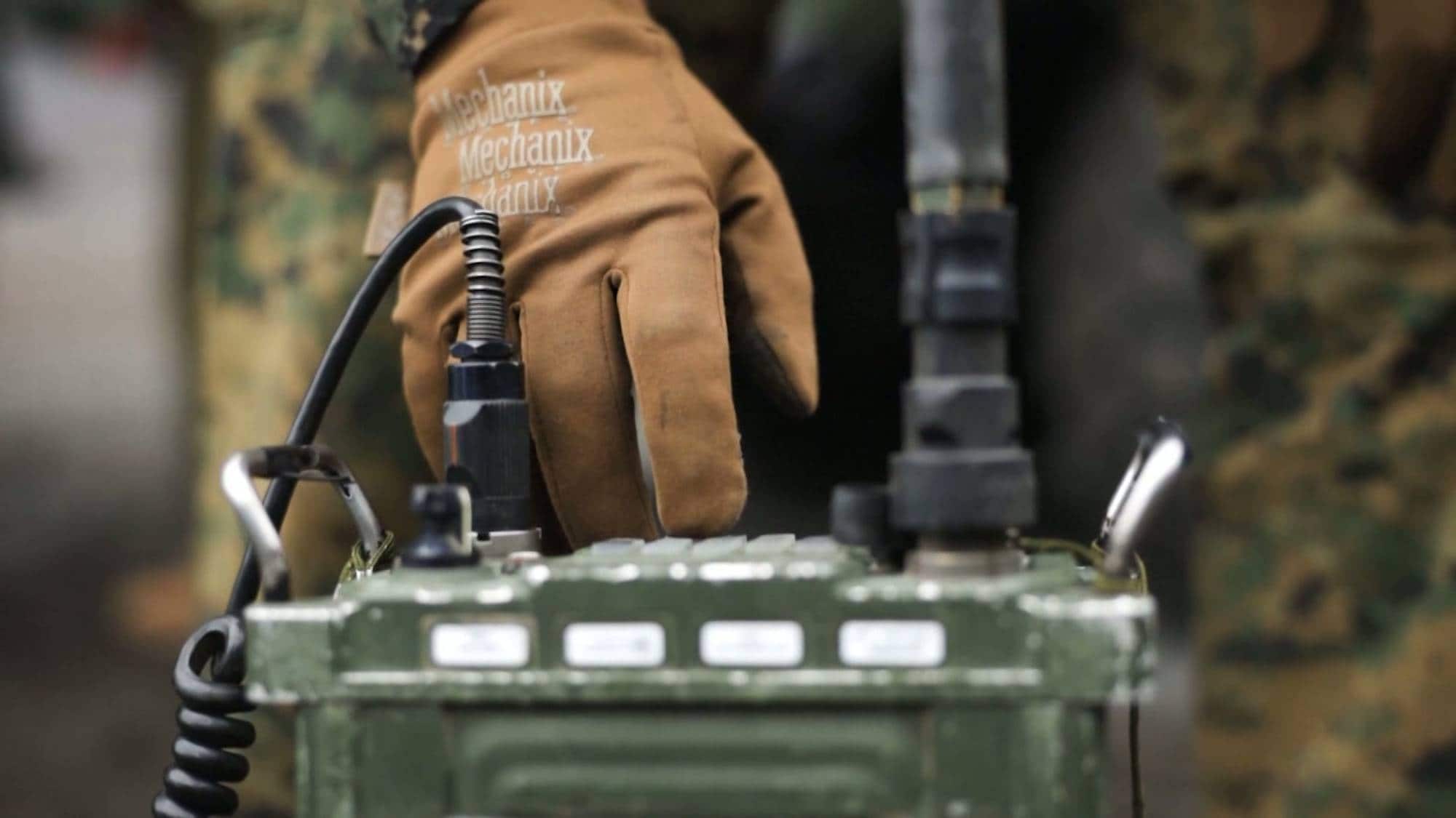 Soldat i kamuflasjeuniform betjener en militær radio med en brun hanske. (Bildebeskrivelsen er laget av en KI-tjeneste)