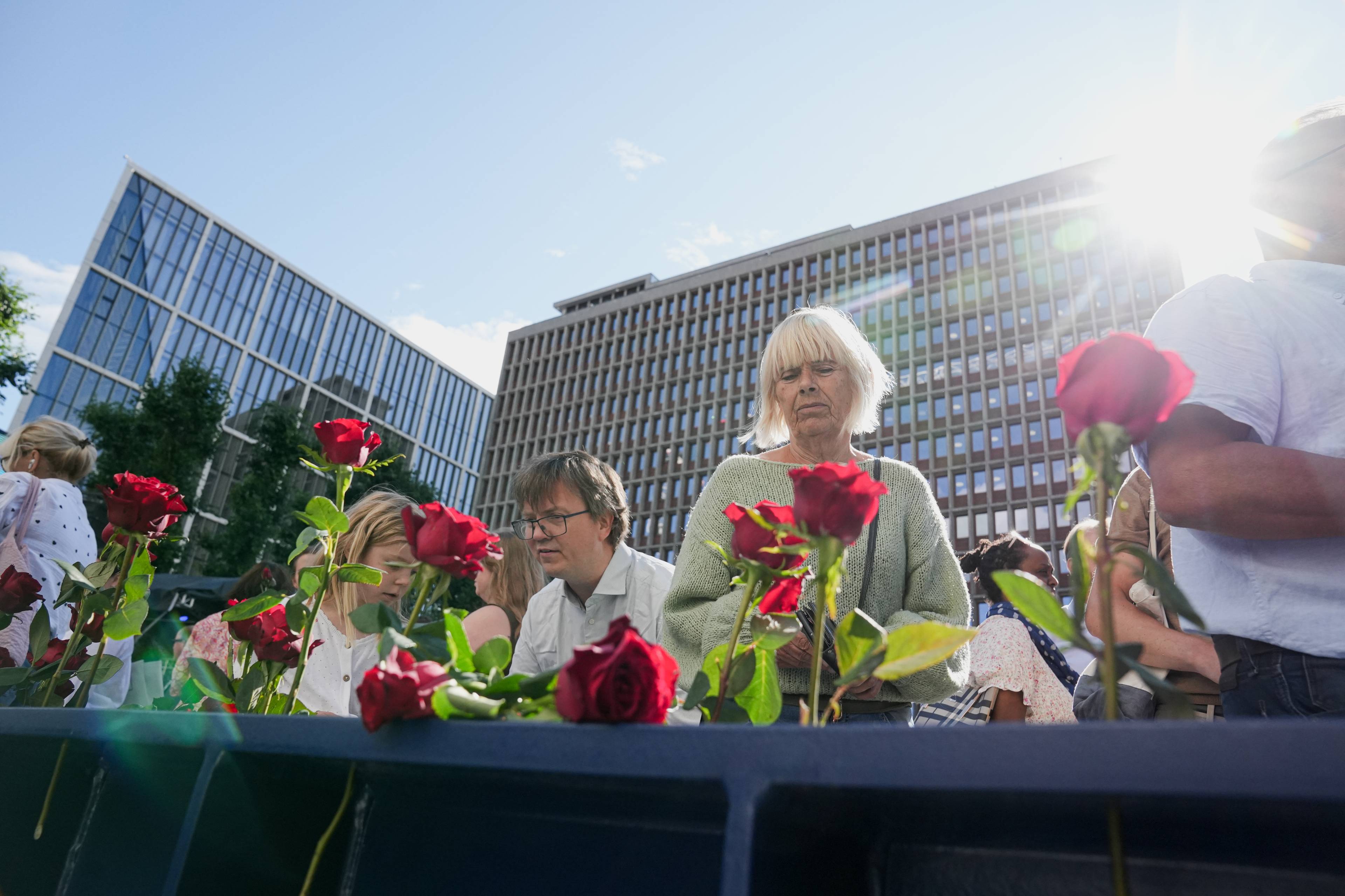 En gruppe folk ser ned på roser foran Regjeringskvartalet