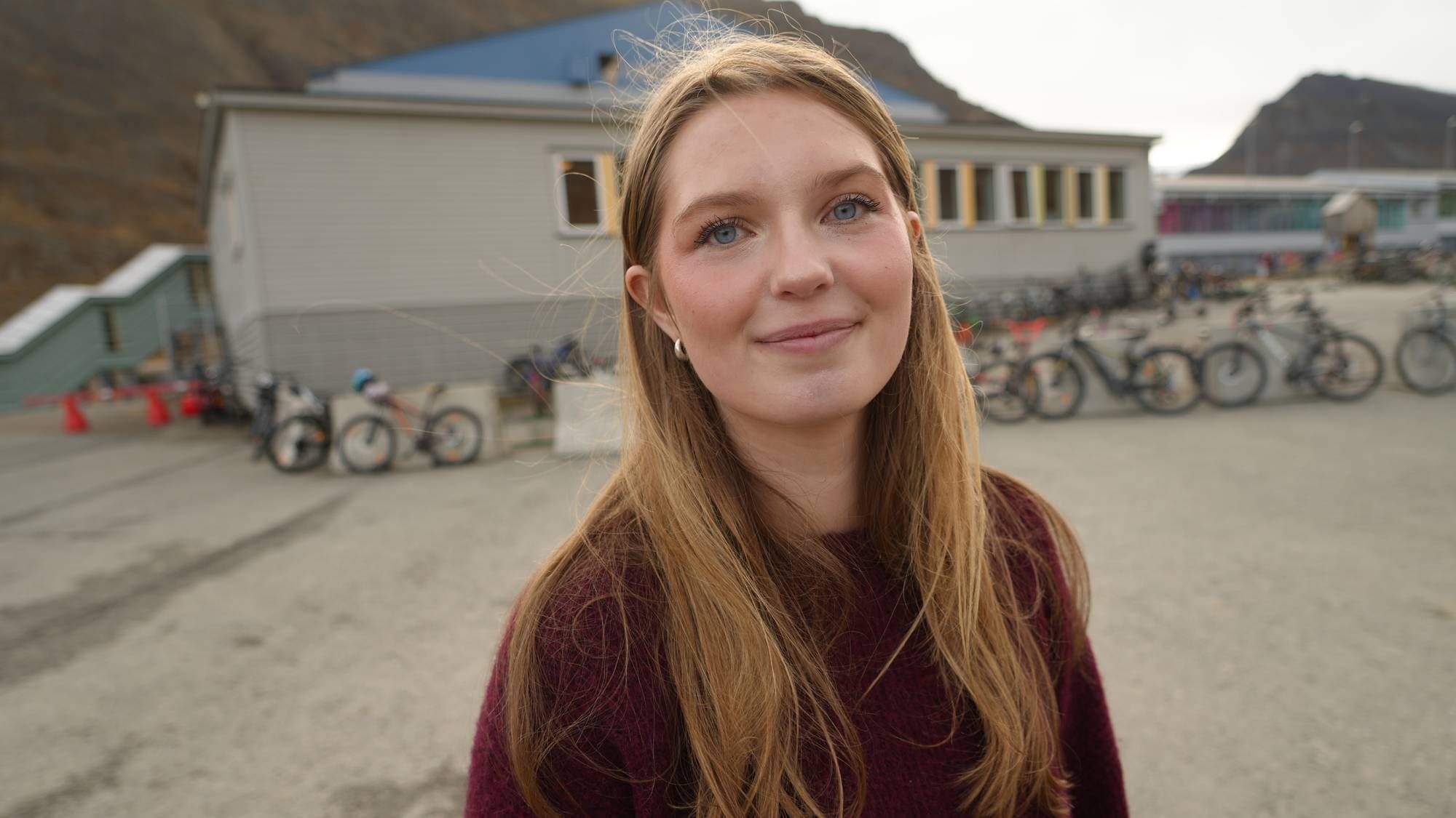 En kvinne ser i kamera. En bygning i bakgrunnen. 