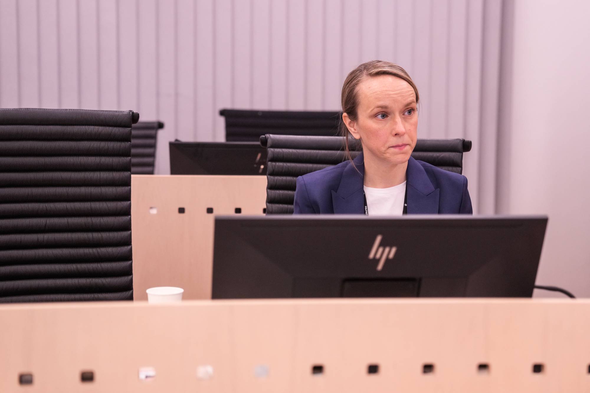 Kvinne i dressjakke sitter ved en kontorpult med en PC-skjerm foran seg i et møterom. (Bildebeskrivelsen er laget av en KI-tjeneste)
