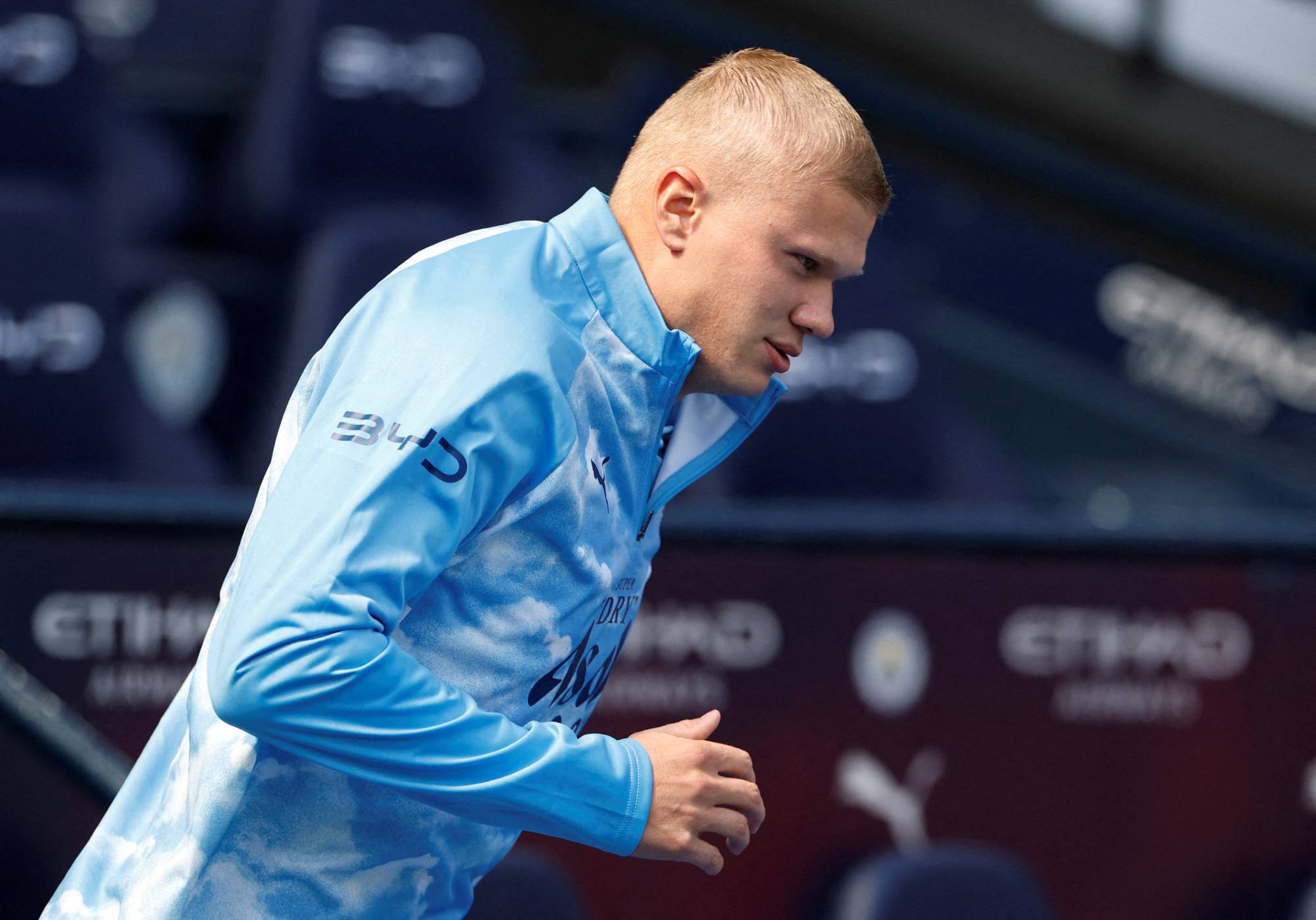 Erling Braut Haaland i lyseblå treningsjakke på en fotballstadion. (Bildebeskrivelsen er laget av en KI-tjeneste)