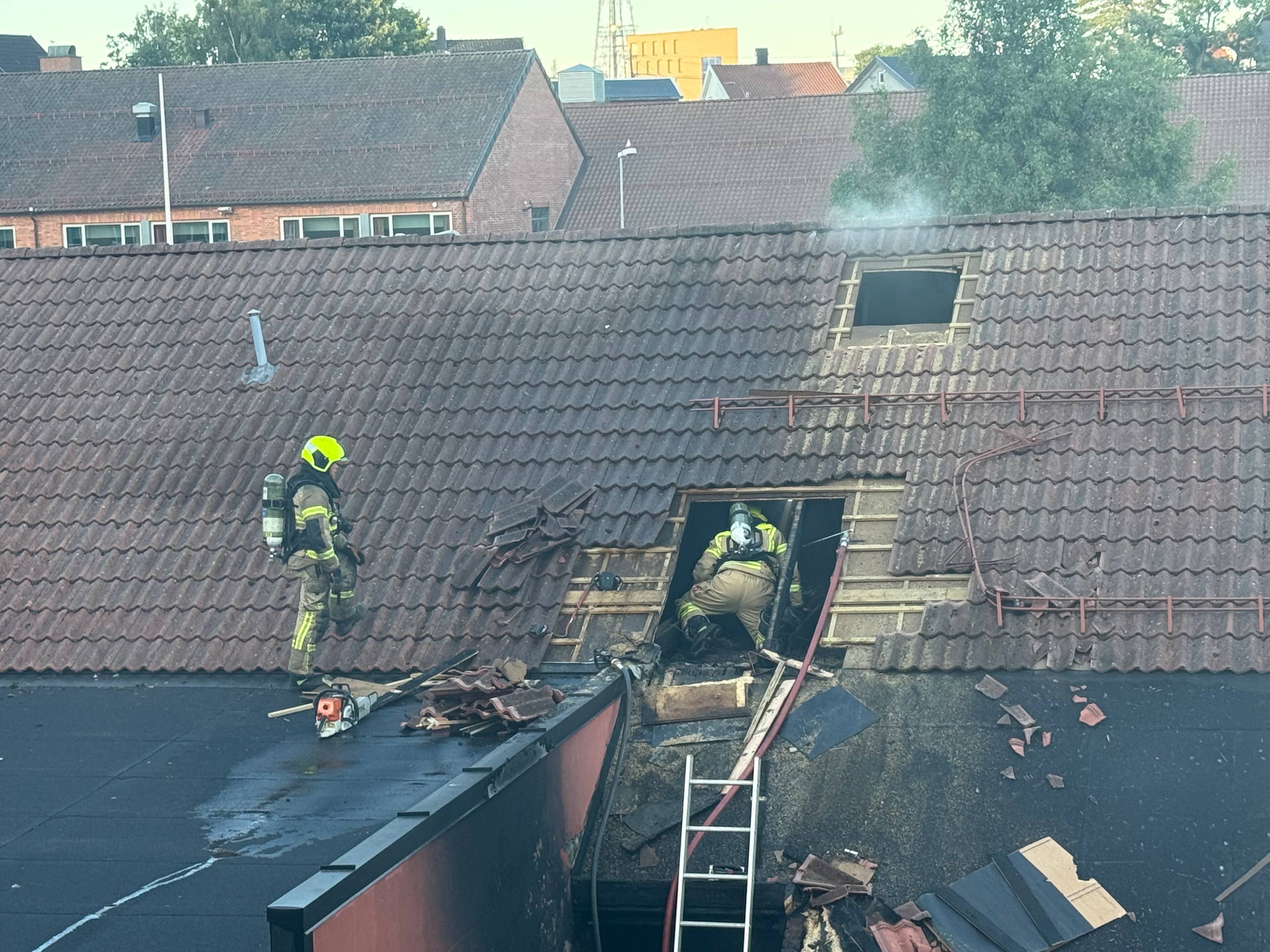 Brannvesenet arbeider med slukkingsarbeid på et tak etter en brann i en bygning. (Bildebeskrivelsen er laget av en KI-tjeneste)