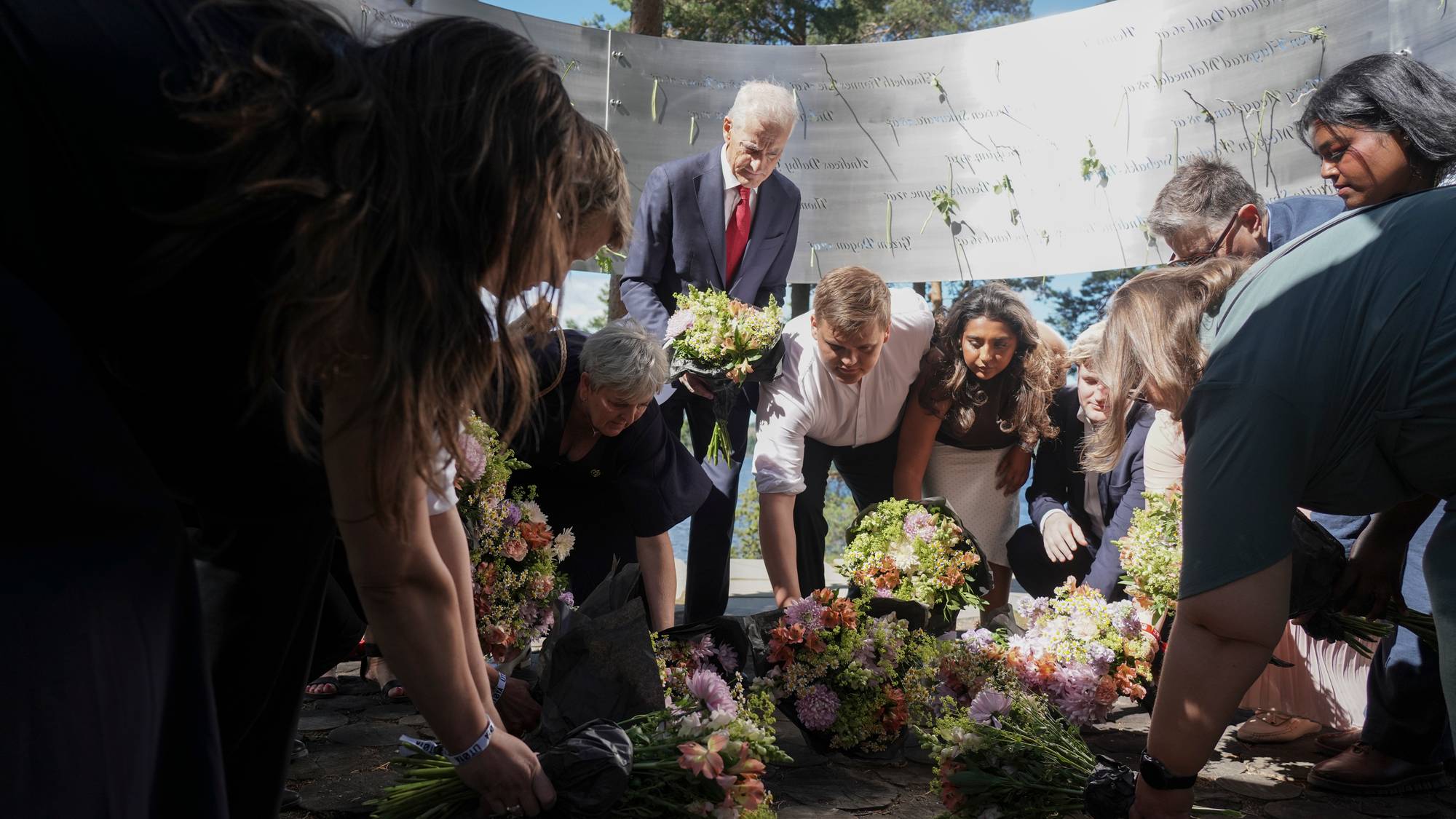 Personer legger ned blomster ved minnesmerket på Utøya under 22. juli-markeringen. (Bildebeskrivelsen er laget av en KI-tjeneste)