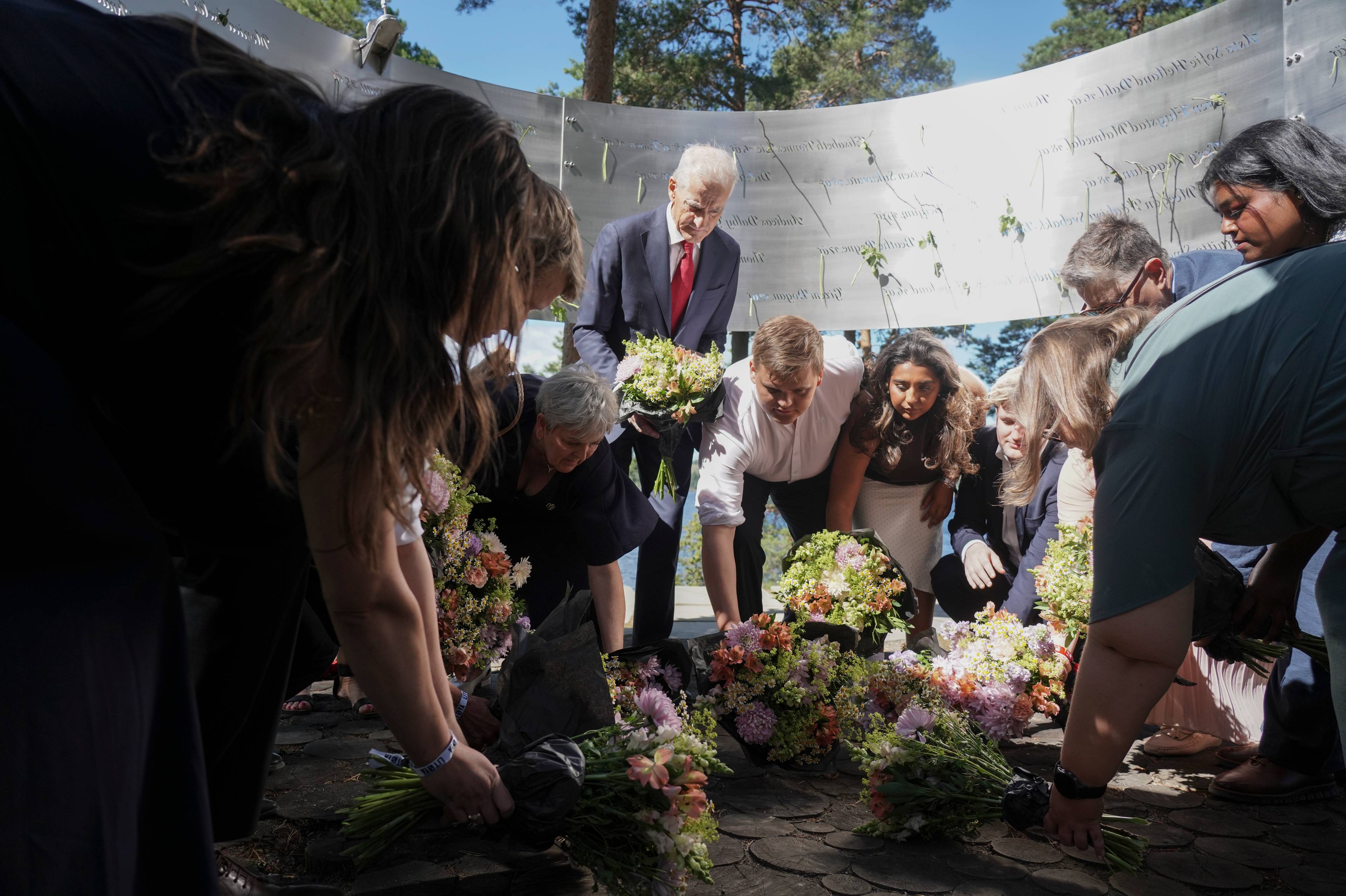 Personer legger ned blomster ved minnesmerket på Utøya under 22. juli-markeringen. (Bildebeskrivelsen er laget av en KI-tjeneste)