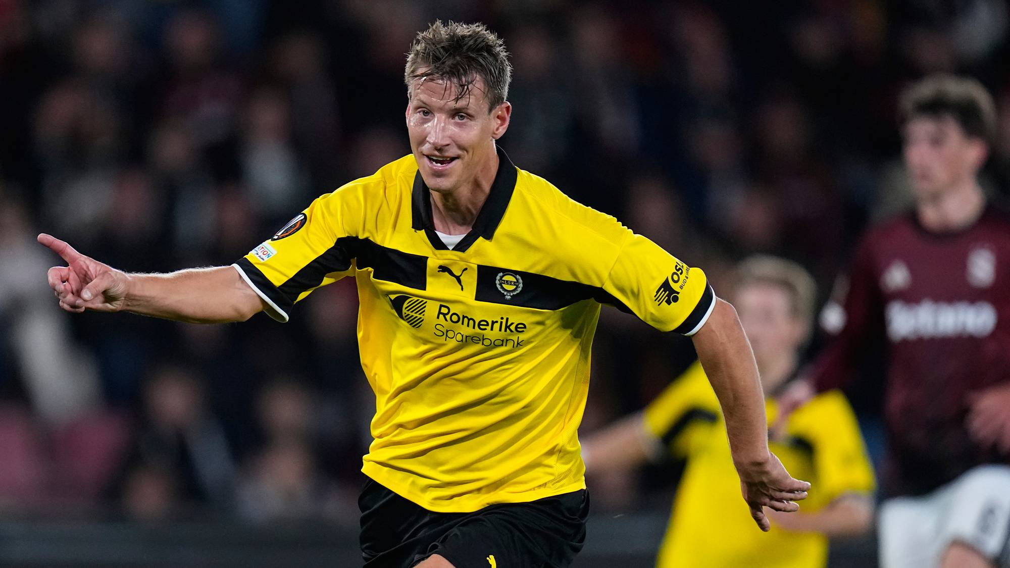 Fotballspiller i gul og svart drakt feirer scoring på banen under en kamp. (Bildebeskrivelsen er laget av en KI-tjeneste)