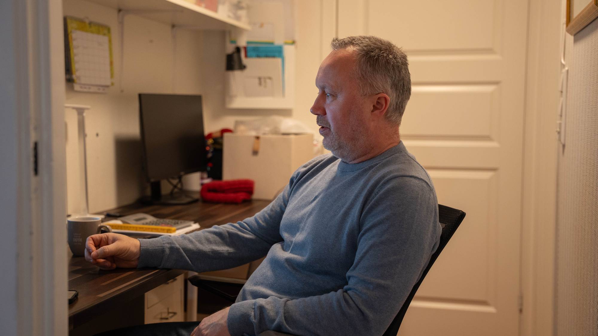 En mann sitter i en kontorstol foran en datamaskin i en smal gang