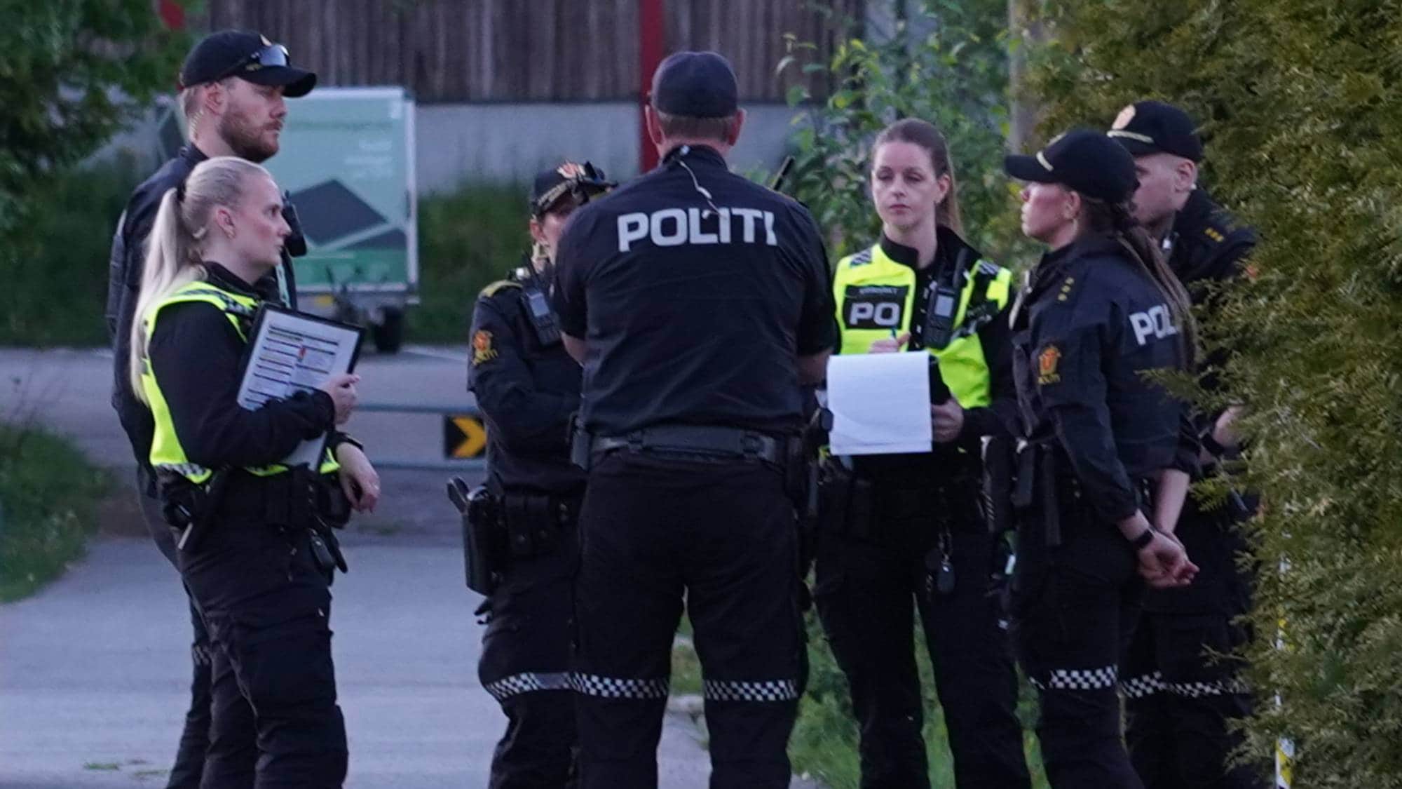 Politi samlet på en vei med to patruljebiler parkert. En gruppe politibetjenter står i en samling og snakker sammen (Bildebeskrivelsen er laget av en KI-tjeneste)