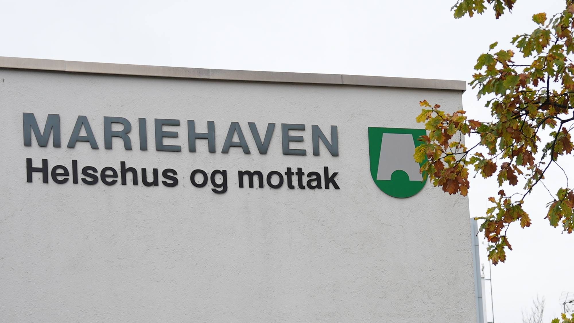 En hvit fasade med høstgule trær i fogrunnen.